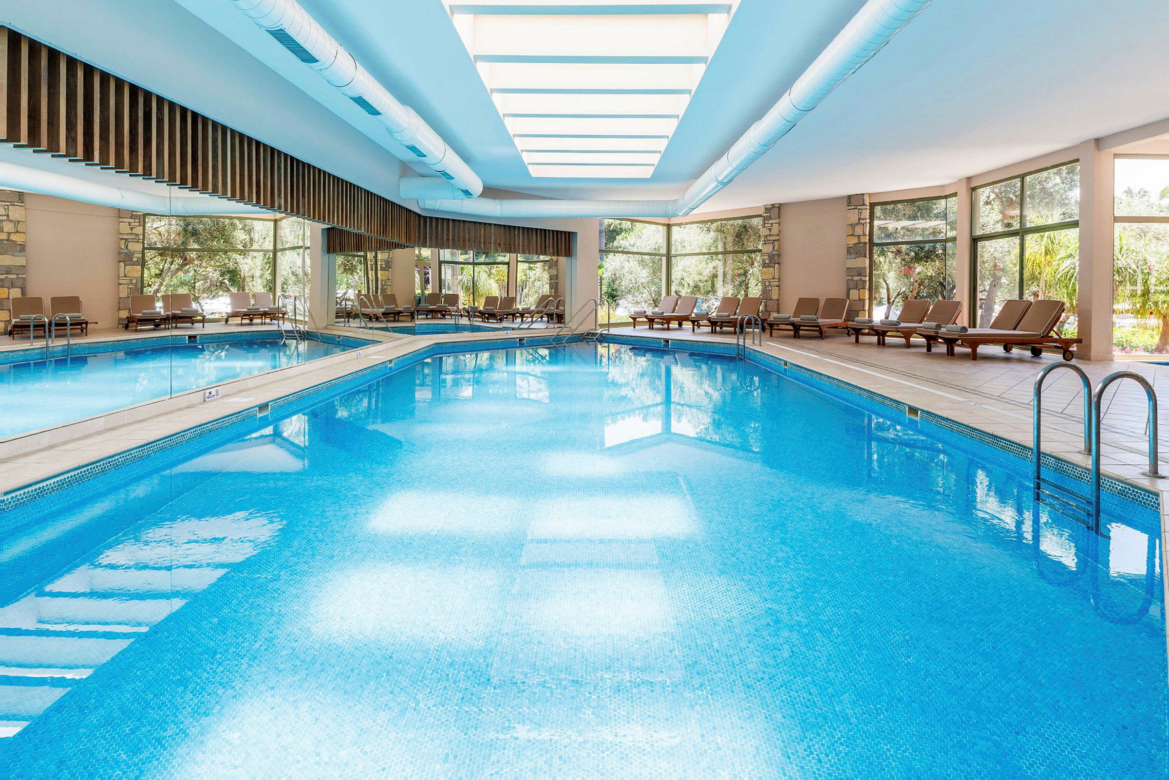 En inomhuspool med solstolar runtom och stora fönster som släpper in dagsljus. (AI-genererad text)