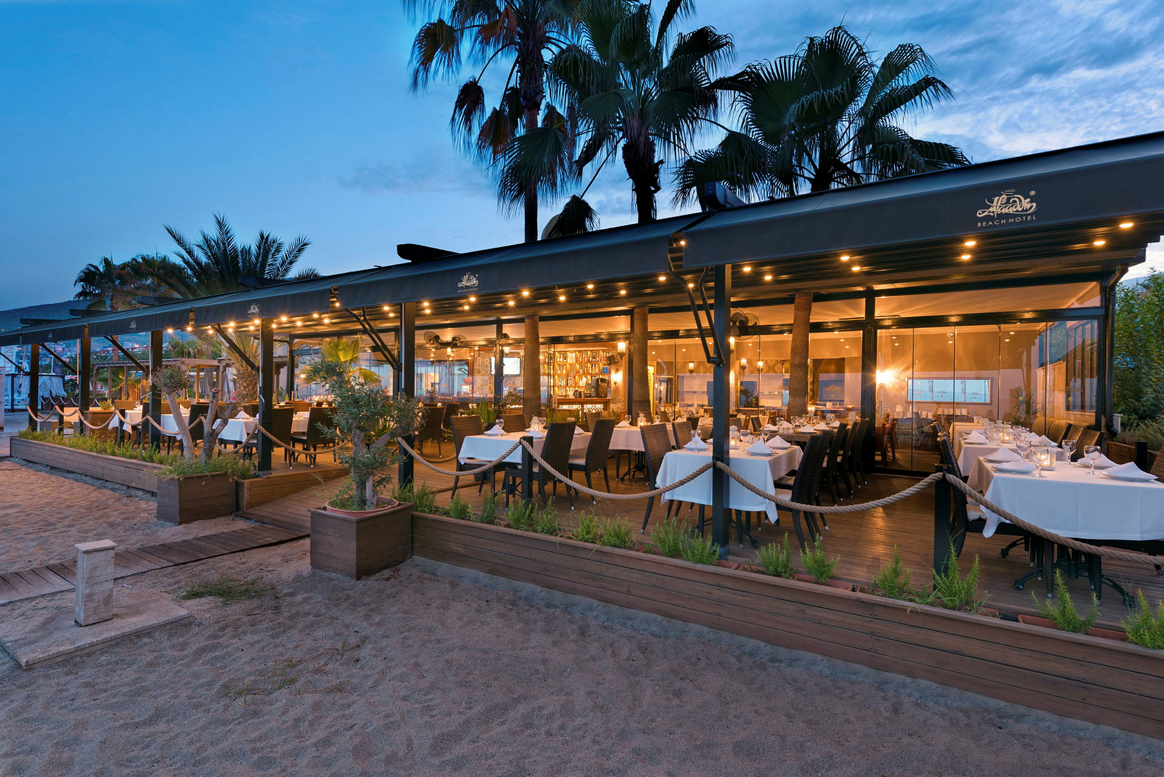 En restaurang vid stranden med vita dukar på kvällstid. (AI-genererad text)