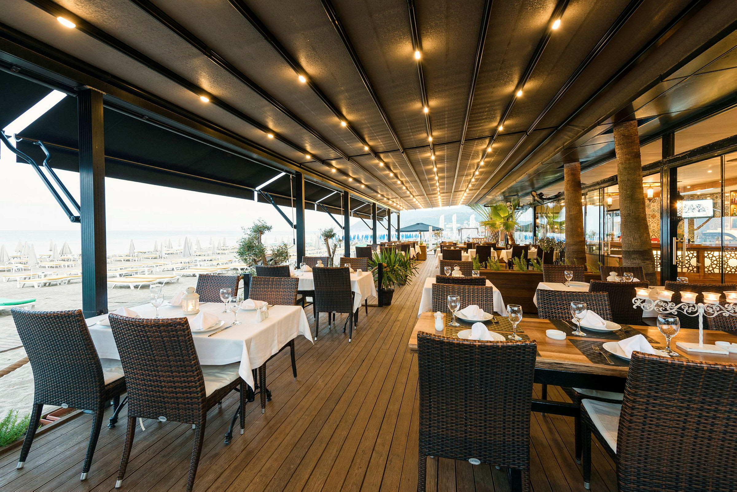 En utomhusrestaurang med dukade bord och stolar nära stranden. (AI-genererad text)