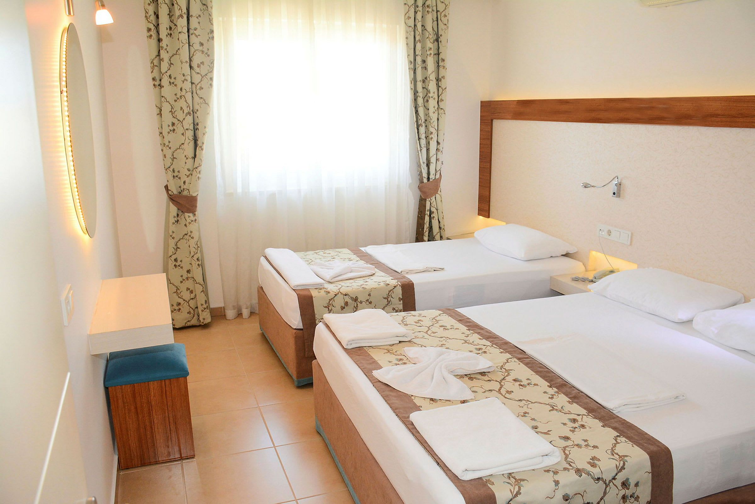 Hotellrum med två enkelsängar, ljusa gardiner och en spegel. (AI-genererad text)