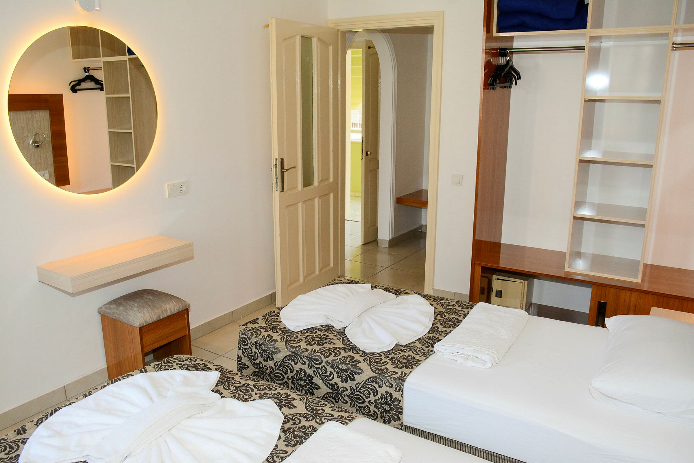 Ett hotellrum med två enkelsängar, en garderob och en rund spegel på väggen. (AI-genererad text)
