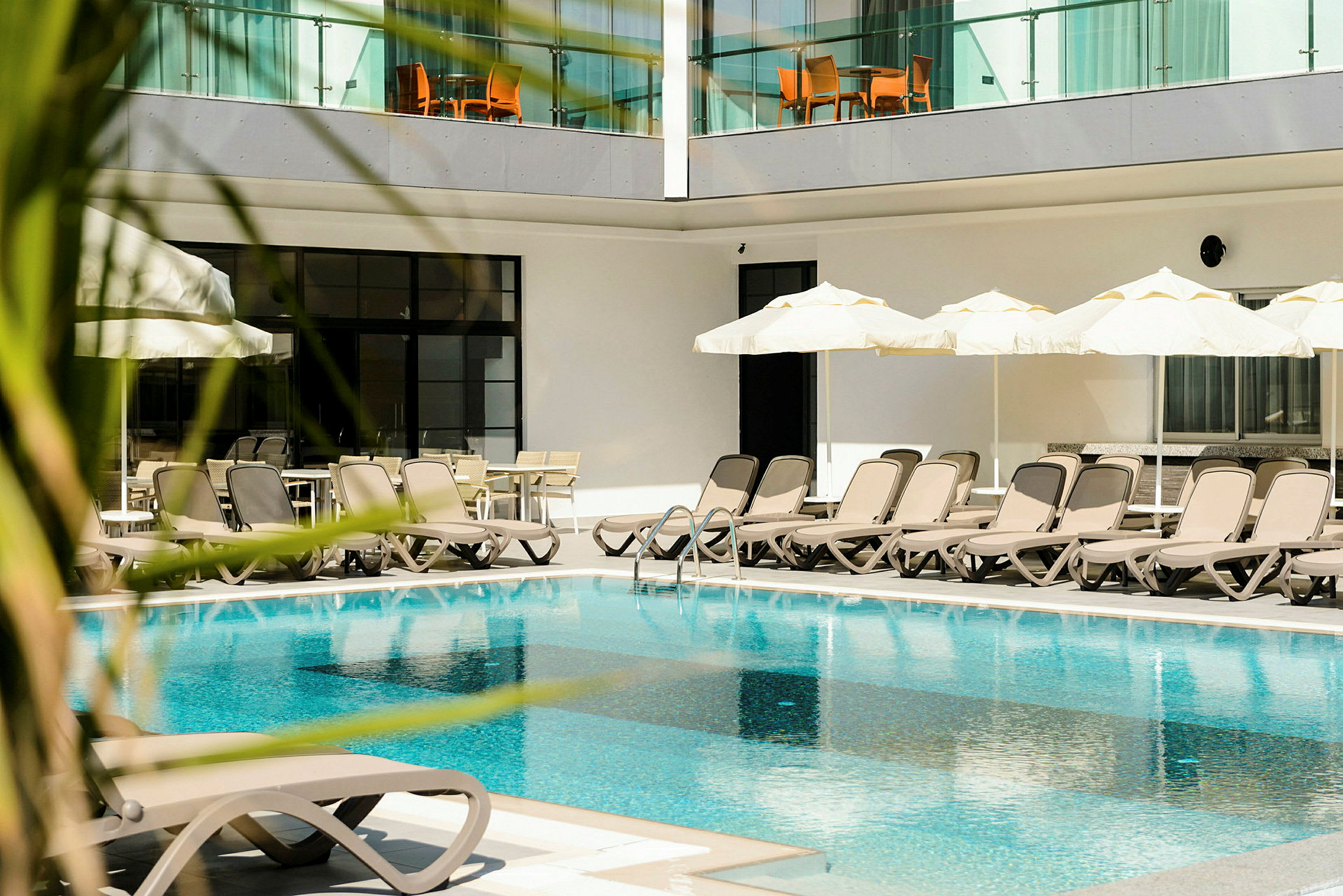 Utomhuspool med solstolar och parasoller vid hotell. (AI-genererad text)