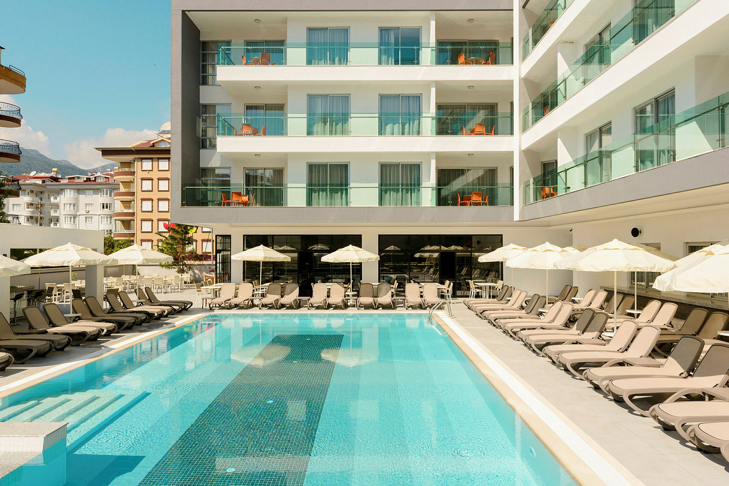 Poolområde med solstolar och parasoller framför ett hotell. (AI-genererad text)
