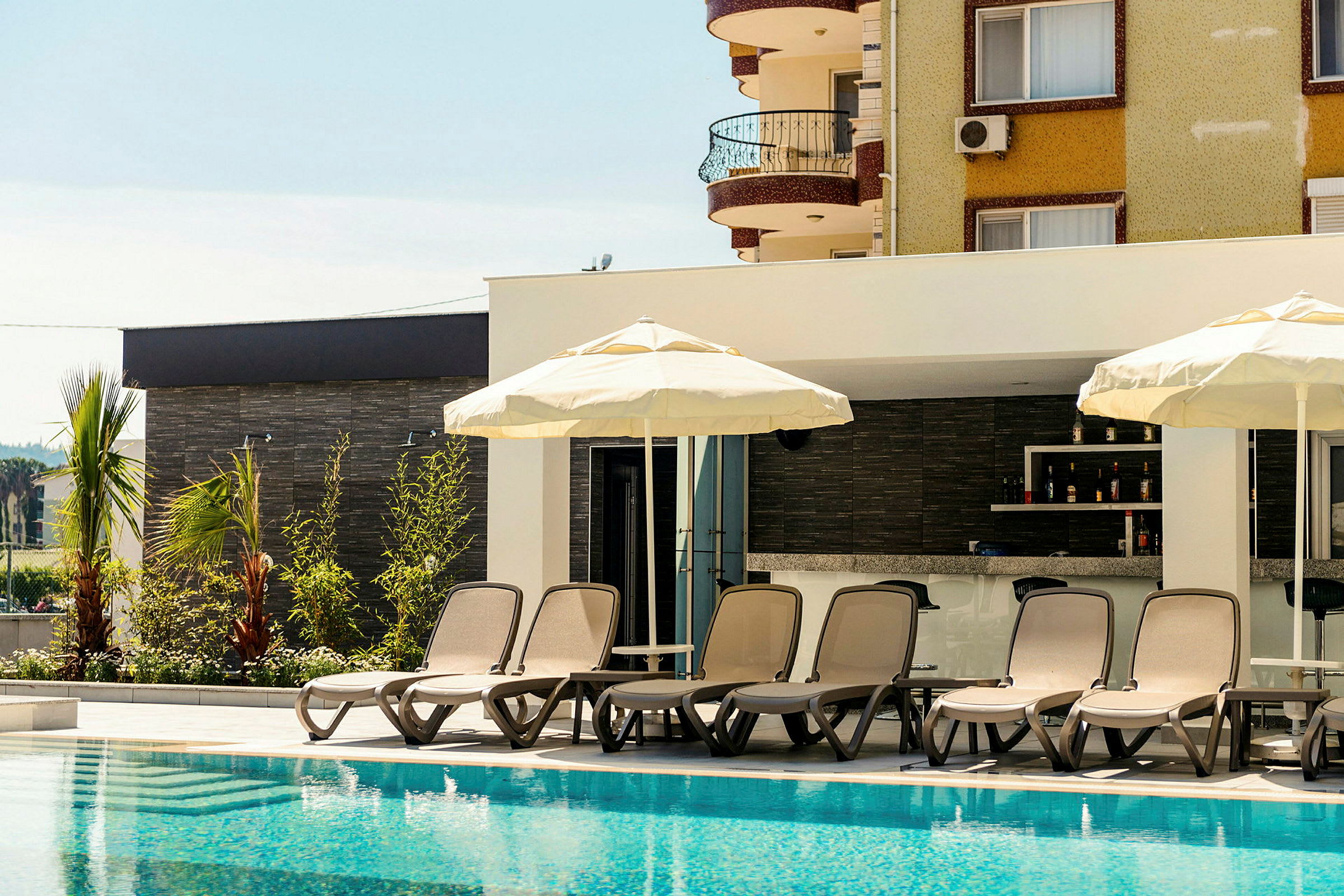 Bild av solstolar och parasoll vid en pool med en byggnad i bakgrunden. (AI-genererad text)