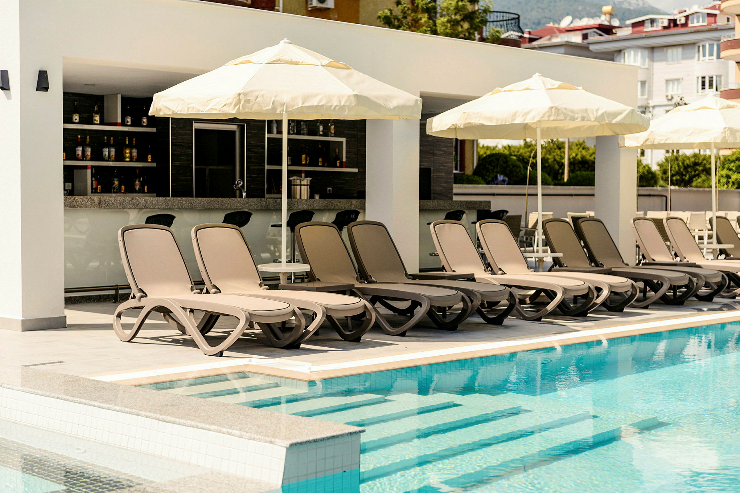Solstolar och parasoller vid en swimmingpool med en bar i bakgrunden. (AI-genererad text)