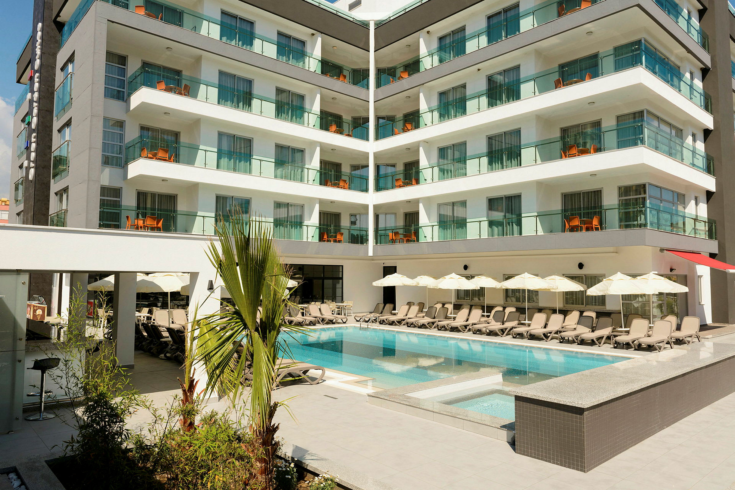 Hotellbyggnad med moderna balkonger och en pool omgiven av solstolar och parasoller. (AI-genererad text)