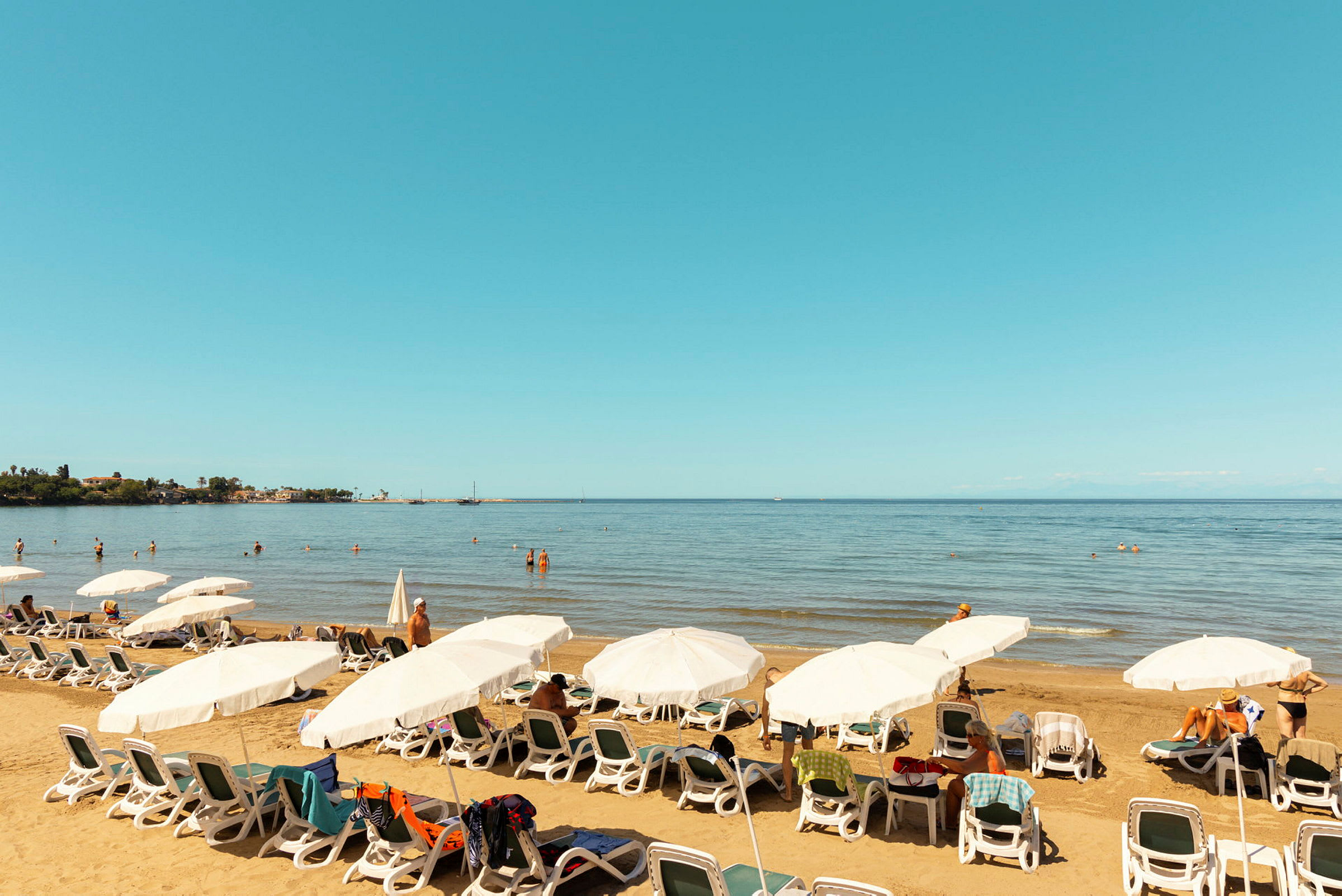 En strand med solstolar och parasoller samt människor som badar i havet. (AI-genererad text)