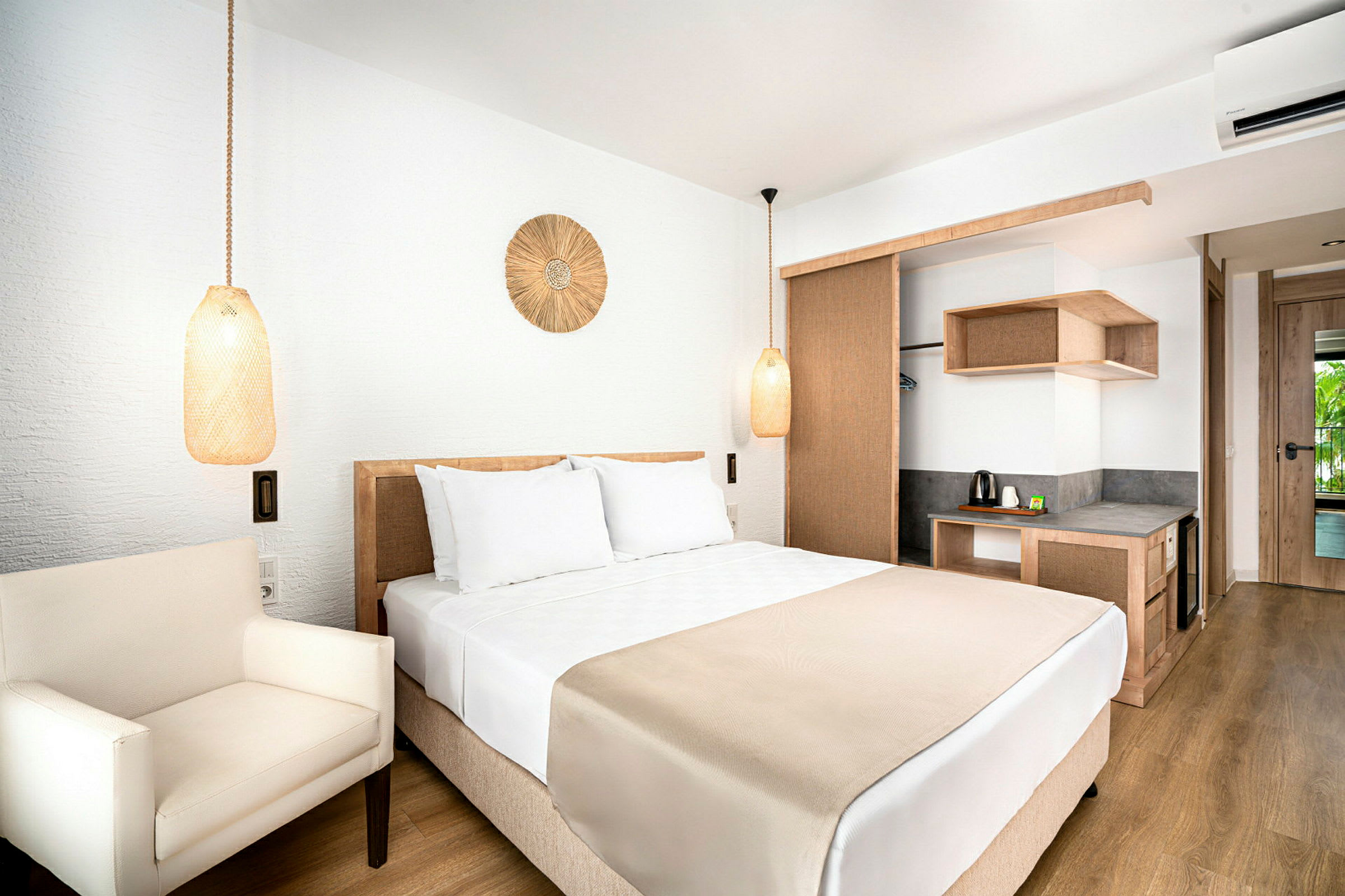 Hotellrum med en dubbelsäng, vita sängkläder och beiga detaljer. I rummet finns en armstol och en skrivhörna med vattenkokare. (AI-genererad text)