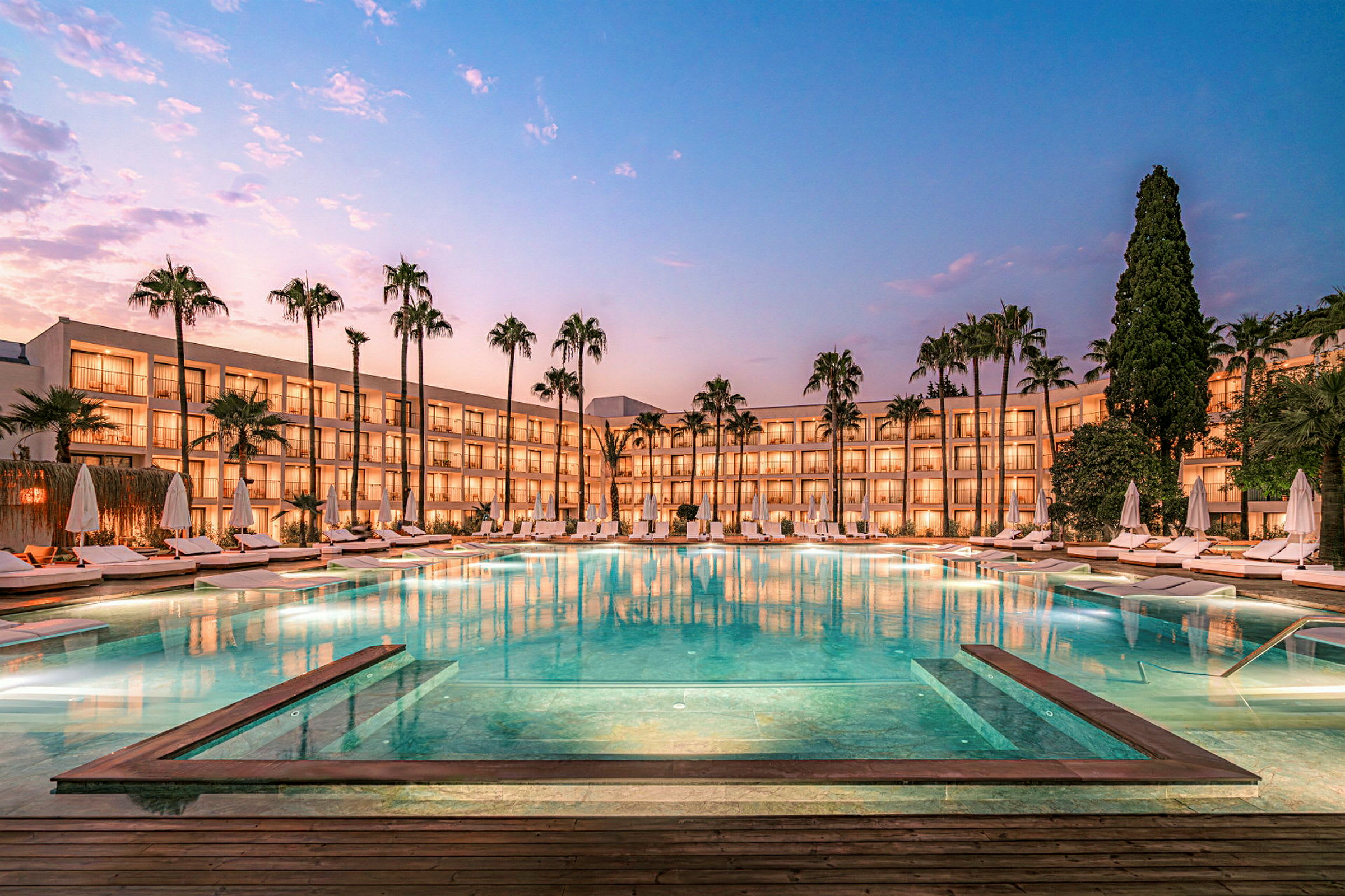 Kvällsbild av hotell med pool och omgivande solstolar. (AI-genererad text)