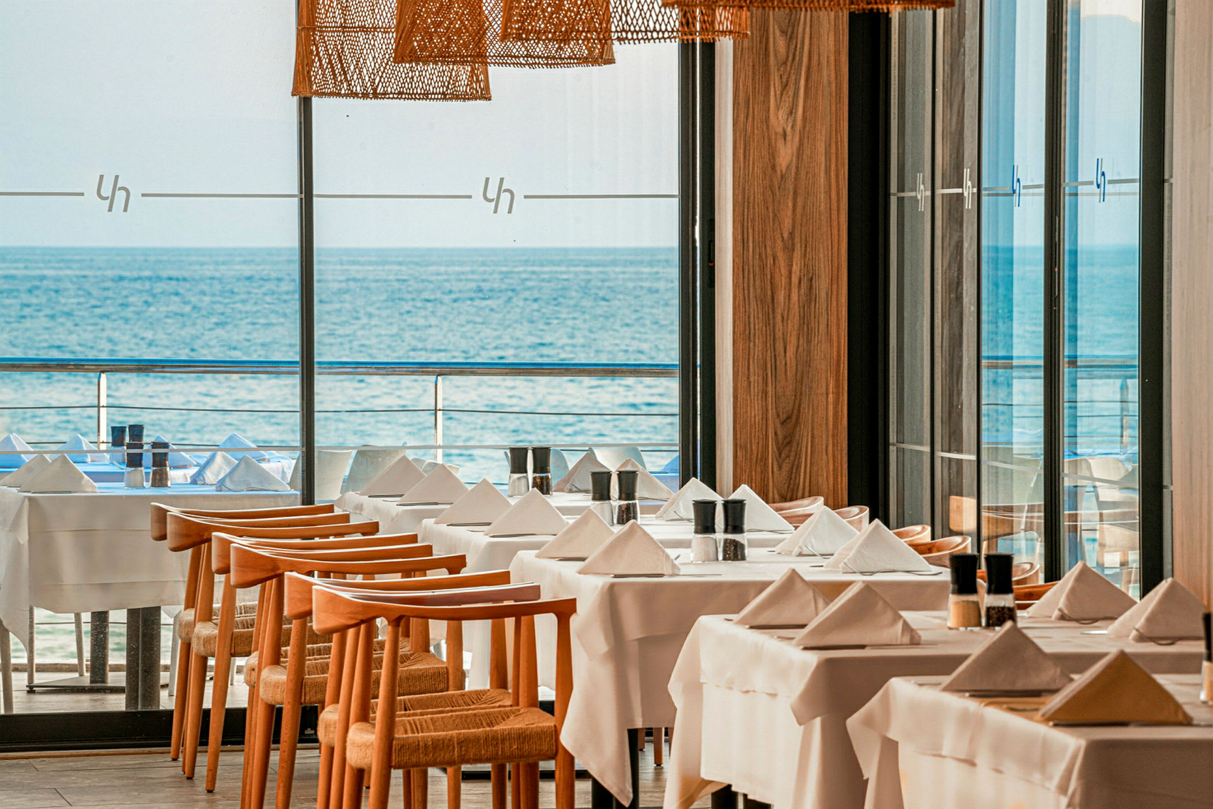 Ett restaurangområde med dukade bord och utsikt över havet. (AI-genererad text)