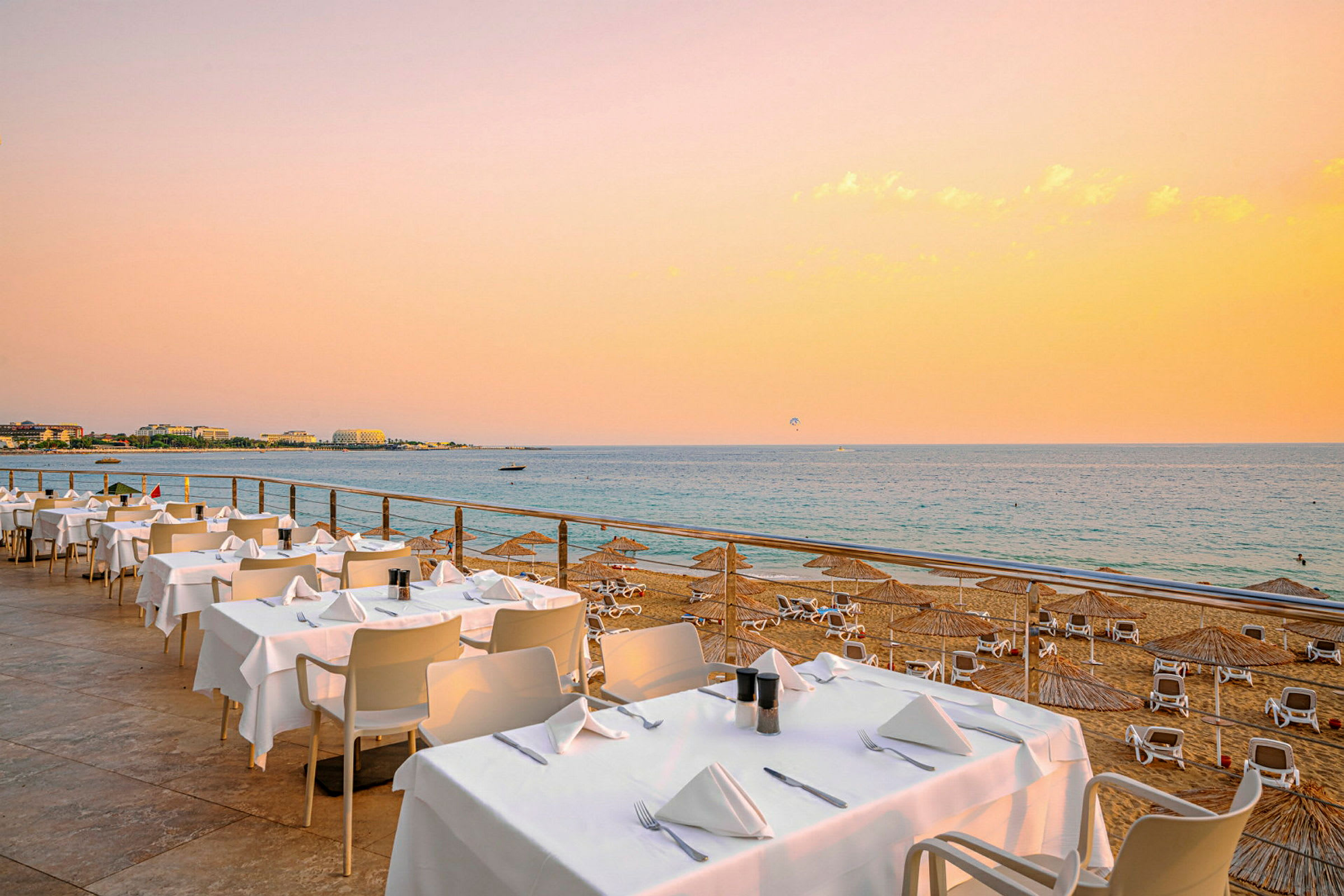 Bild på en strand med solstolar och parasoller, samt en restaurang med dukade bord vid havet. (AI-genererad text)