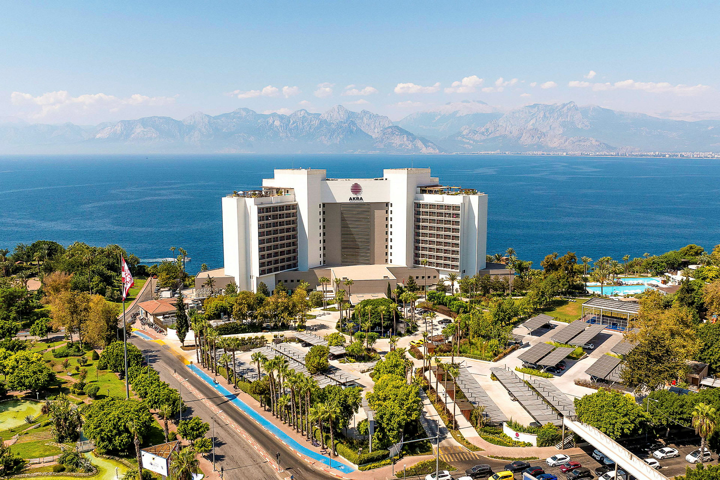 Hotellbyggnad med utsikt över havet, omgiven av träd och parkeringsområde. (AI-genererad text)