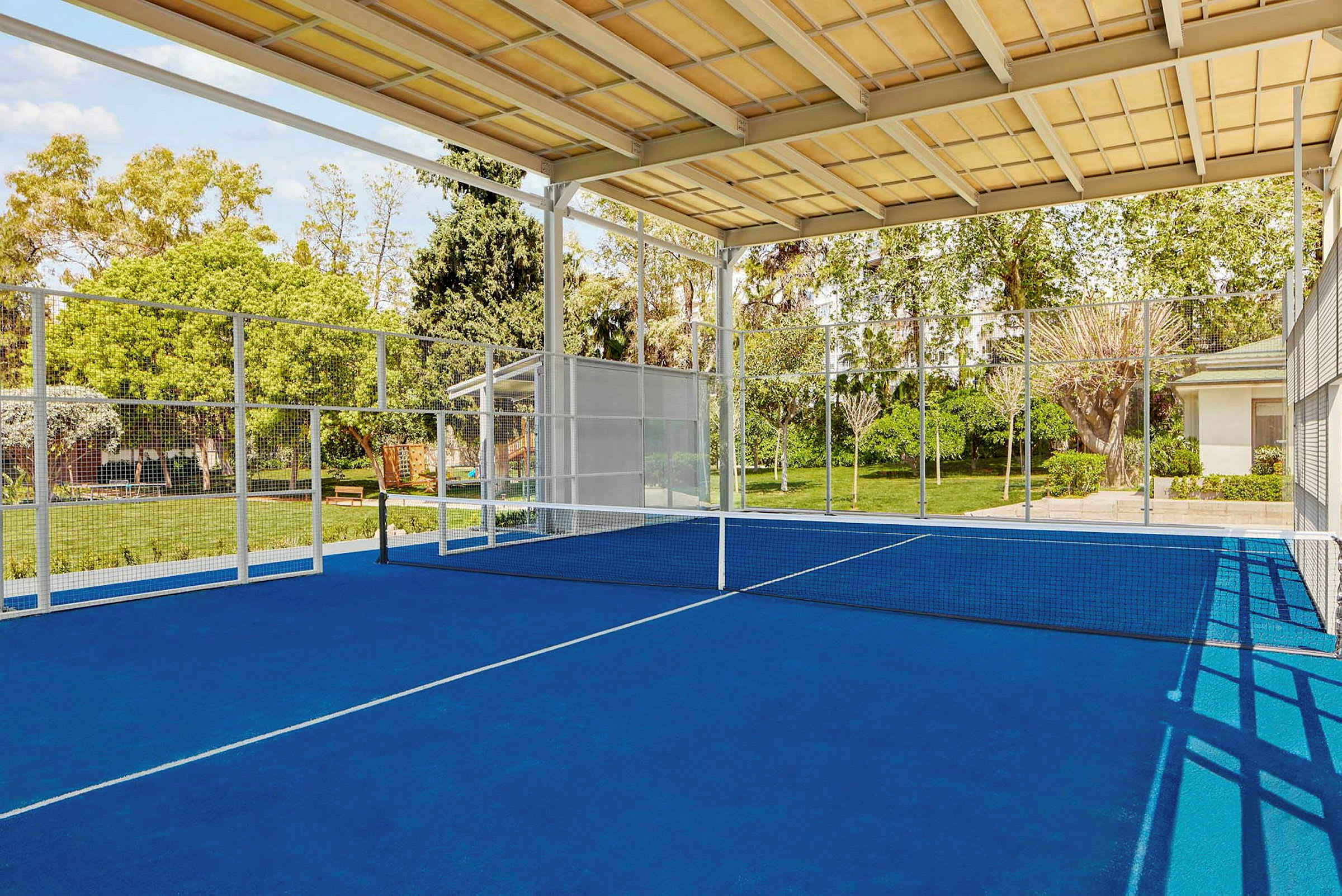 En padelbana med blått underlag, nät och omgivande grönska. (AI-genererad text)
