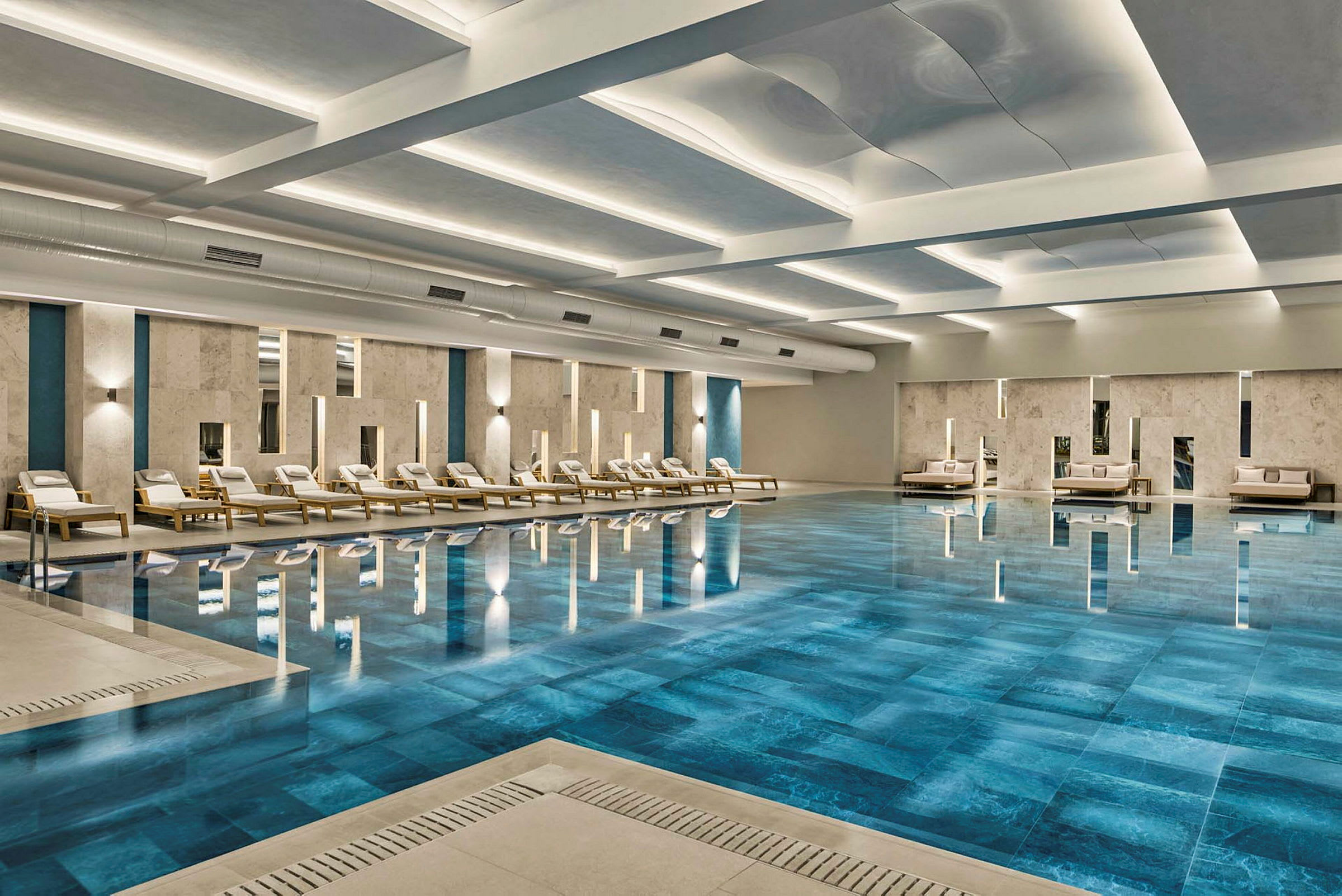 En inomhuspool omgiven av solstolar och sittmöbler, med modernt designad inredning. (AI-genererad text)