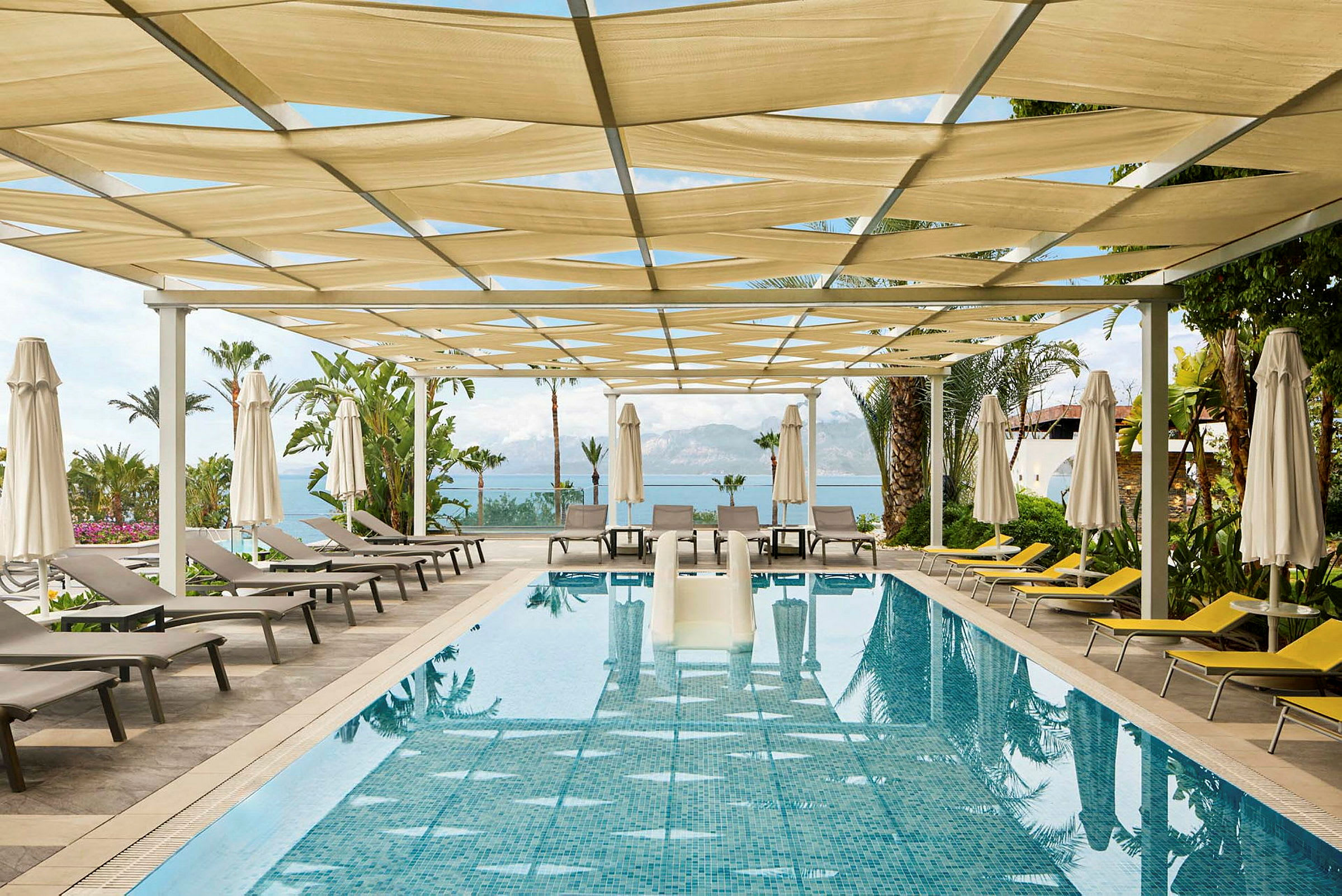 En pool med solstolar och parasoller under en pergola. (AI-genererad text)