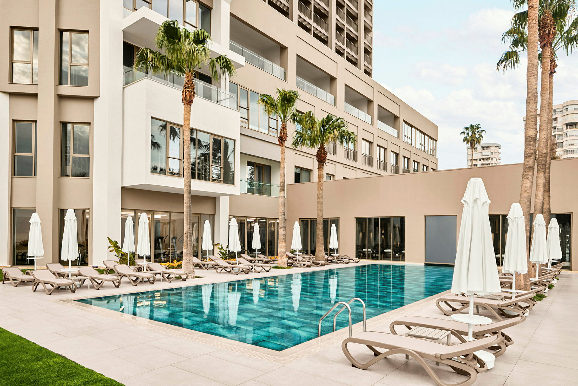 Ett hotellområde med en pool, solstolar och parasoller omgivna av palmer. (AI-genererad text)