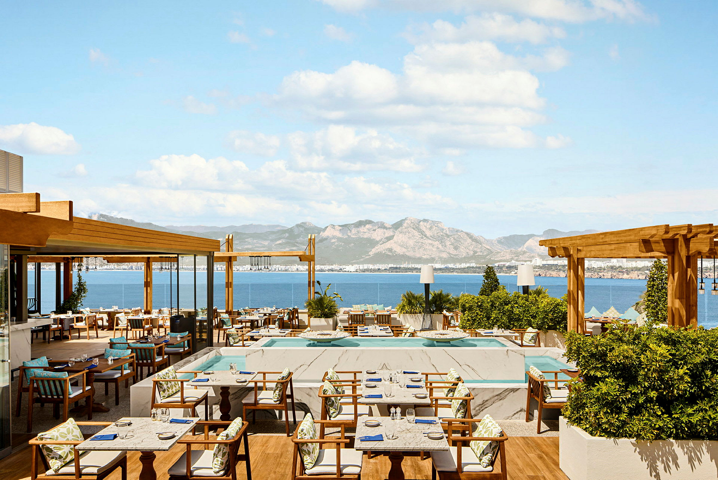 En restaurangterrass med havsutsikt och berg i bakgrunden. (AI-genererad text)