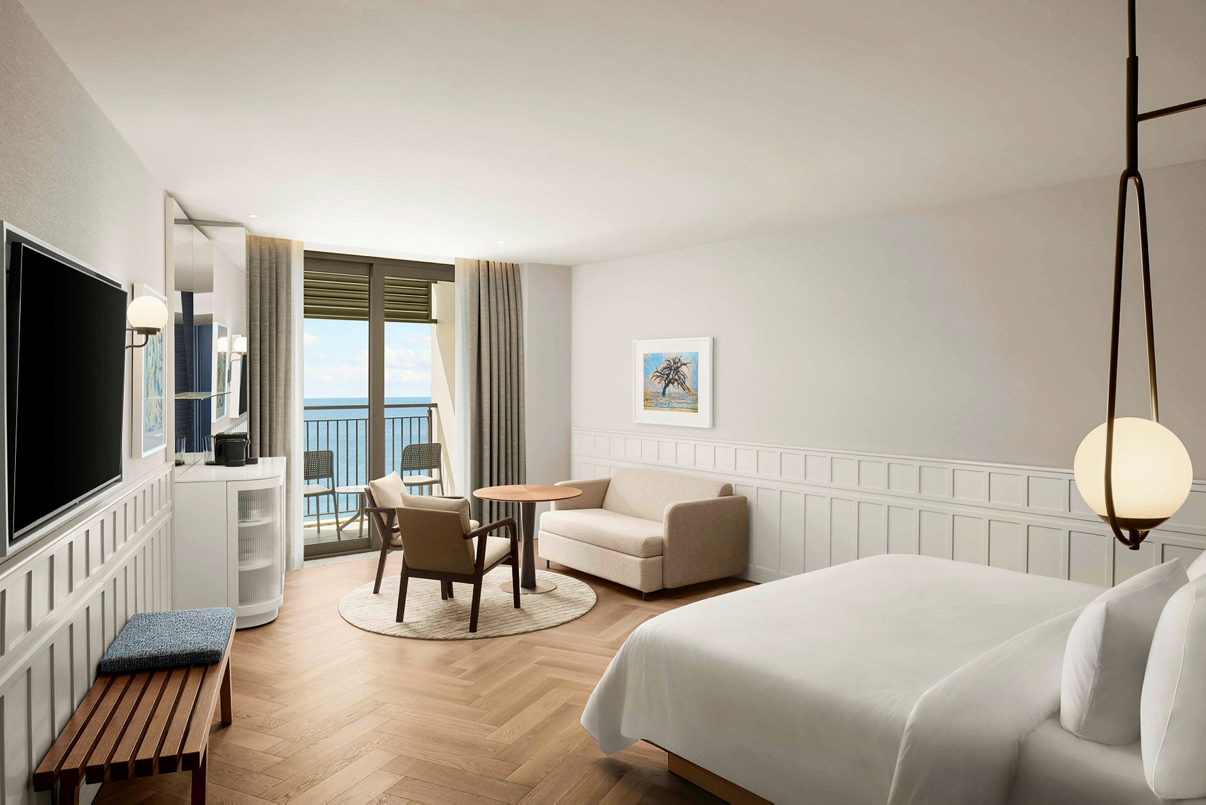 Ett hotellrum med stor säng, sittgrupp och balkong med utsikt över havet. (AI-genererad text)