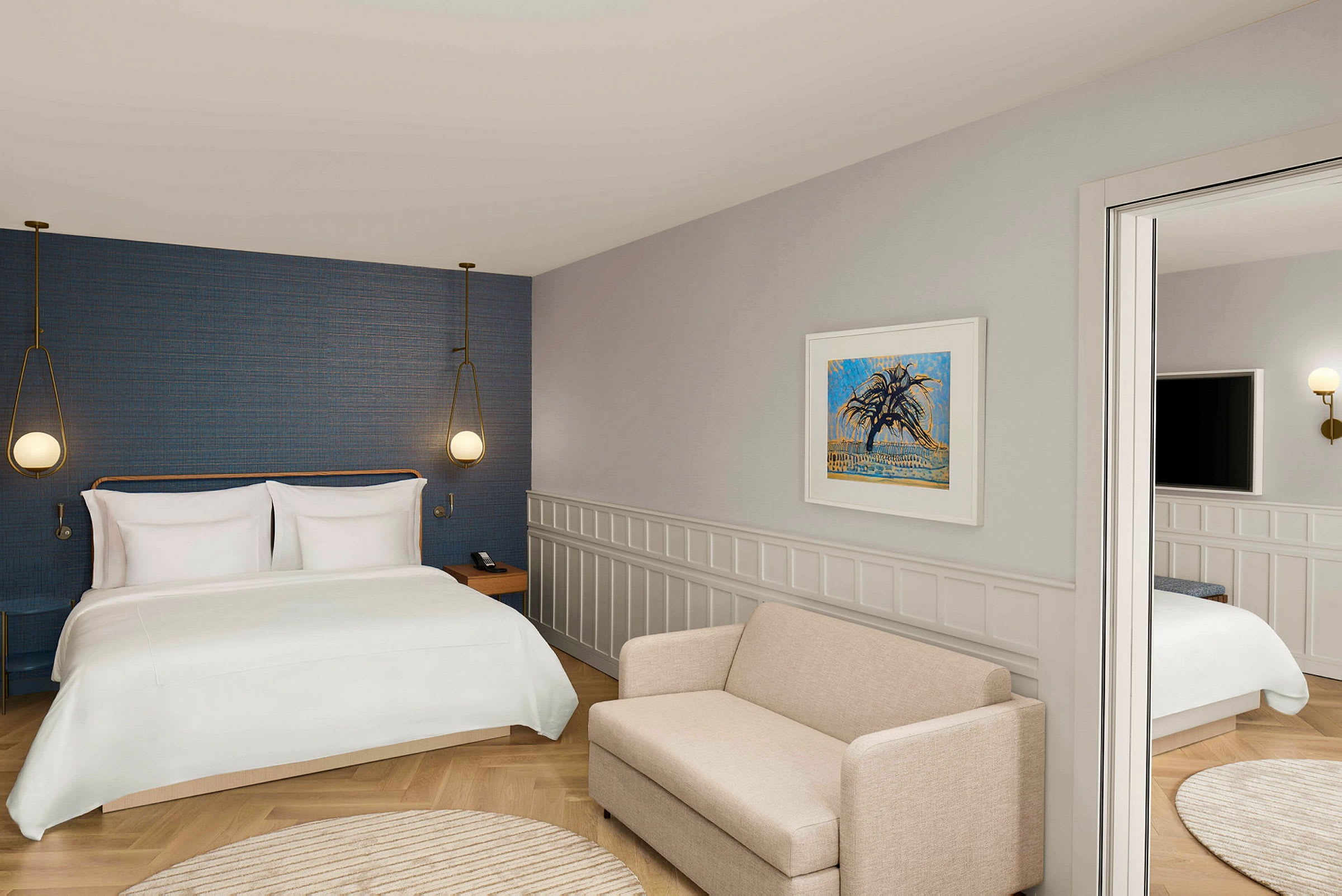 Ett hotellrum med en stor säng, vägglampor, en beige soffa och konst på väggen. (AI-genererad text)