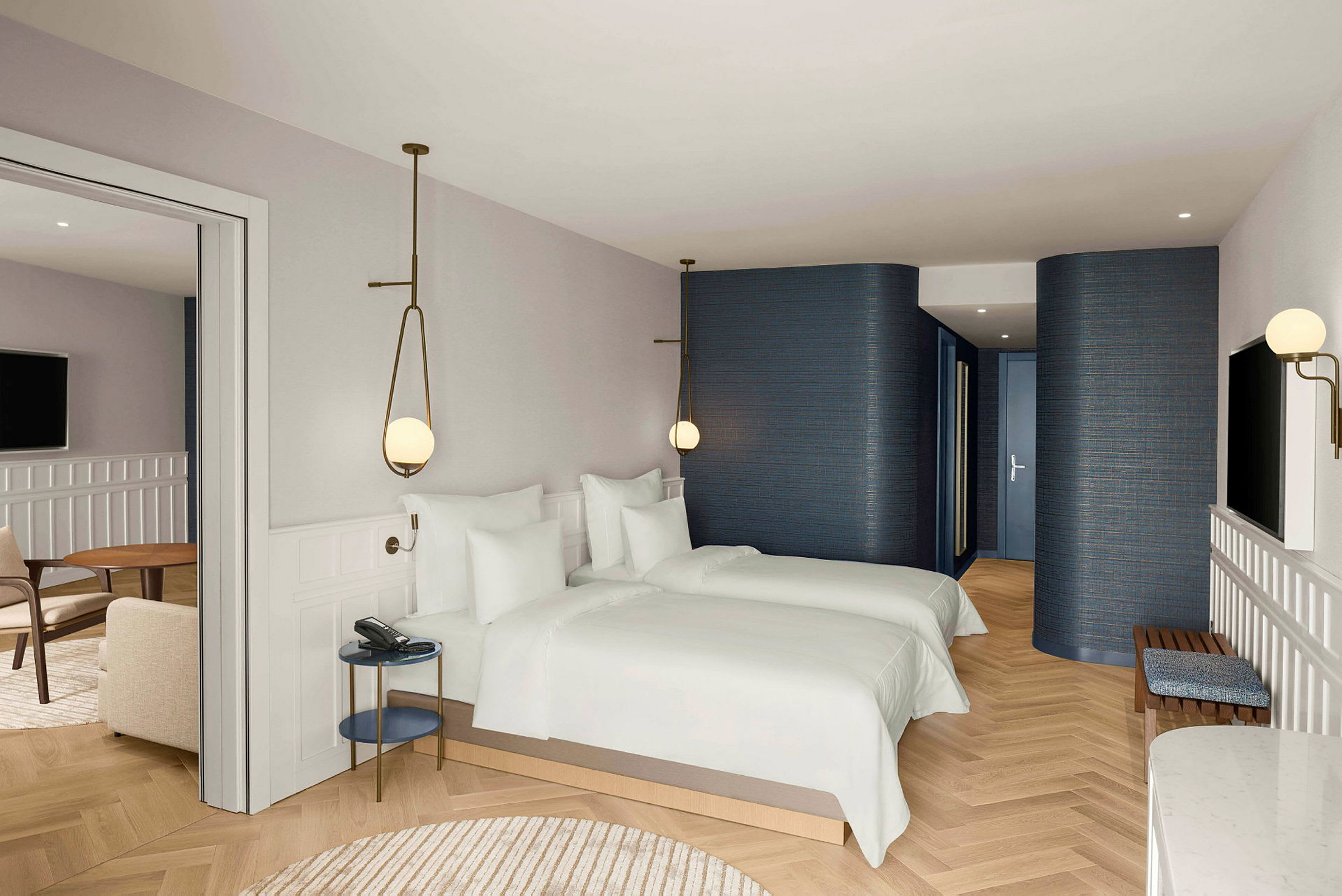 Ett hotellrum med två enkelsängar, ljusa väggar och golv, samt en sittgrupp med bord och stolar. (AI-genererad text)
