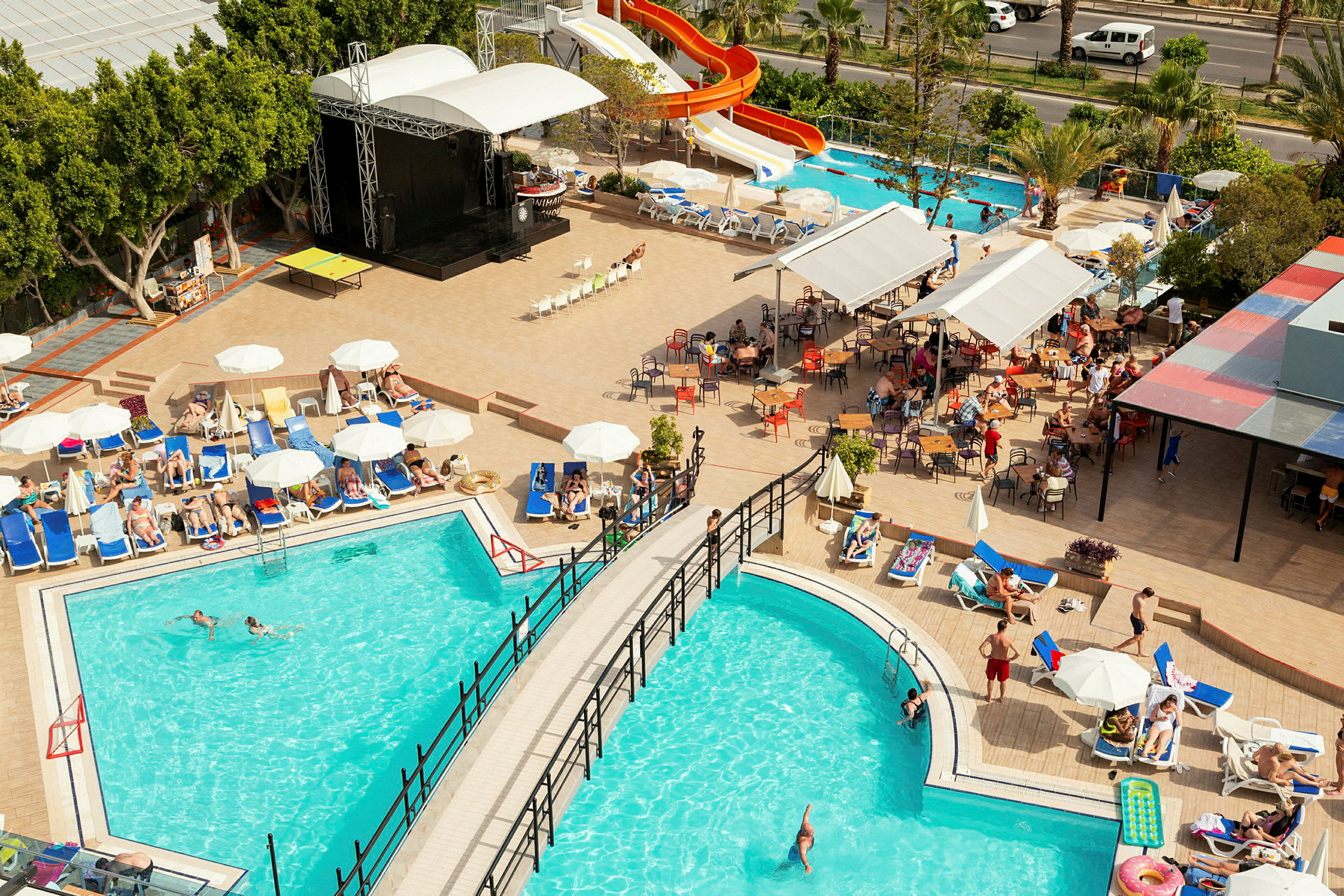 Vy över hotellområde med pooler, solstolar och vattenrutschbana. (AI-genererad text)