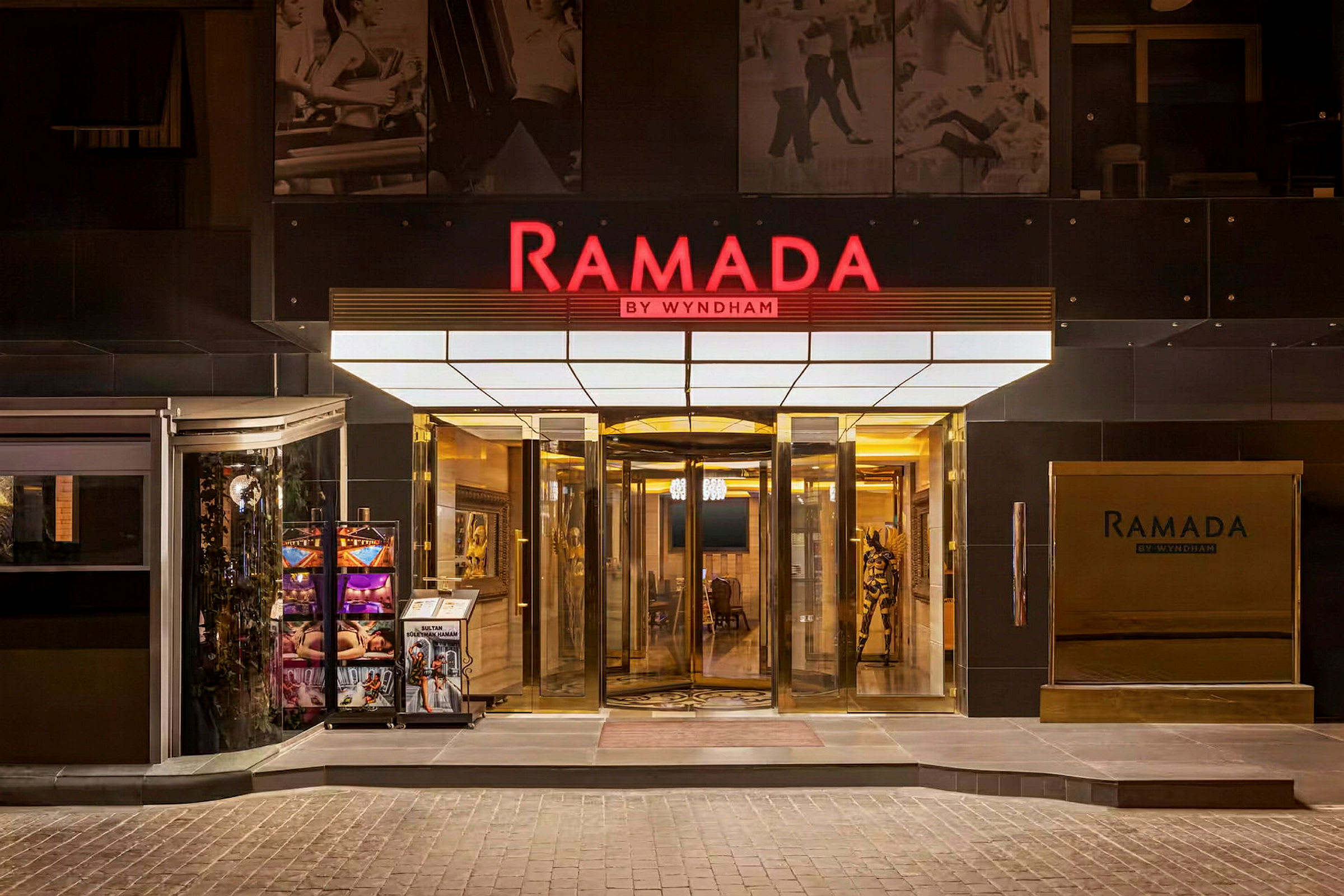 Huvudentrén till hotellkedjan Ramada by Wyndham, med en snurrdörr och skyltar. (AI-genererad text)