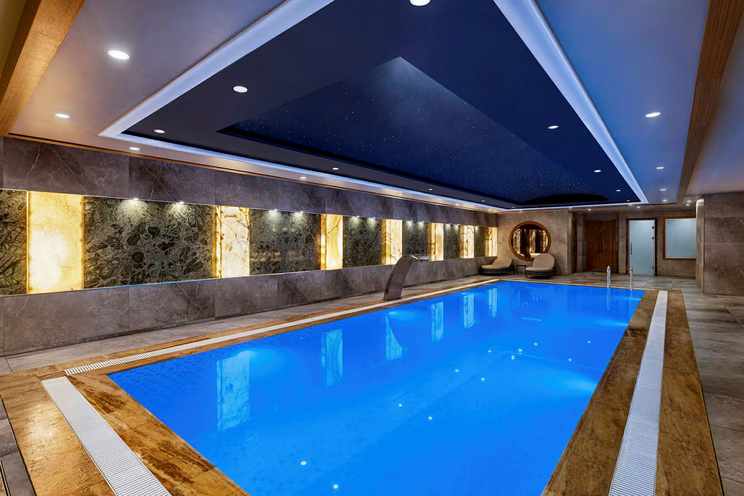 En inomhuspool med blått vatten i en elegant och modern miljö. Väggarna har dekorativa paneler och taket har stjärnliknande lampor. (AI-genererad text)