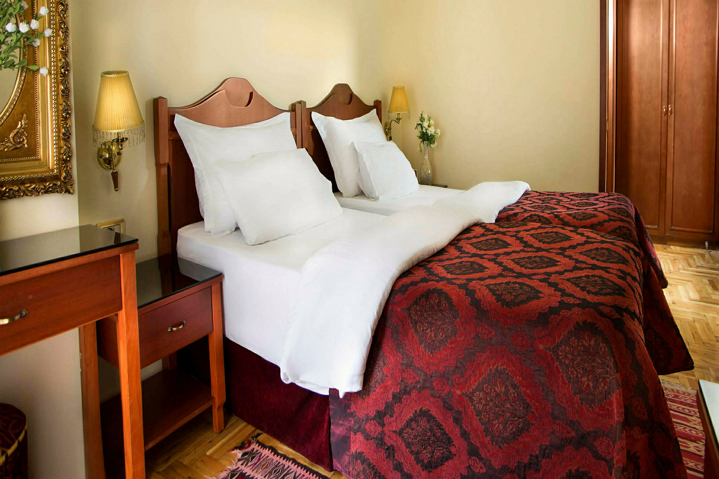 Två enkelsängar med vita lakan och röda överkast i ett hotellrum. (AI-genererad text)