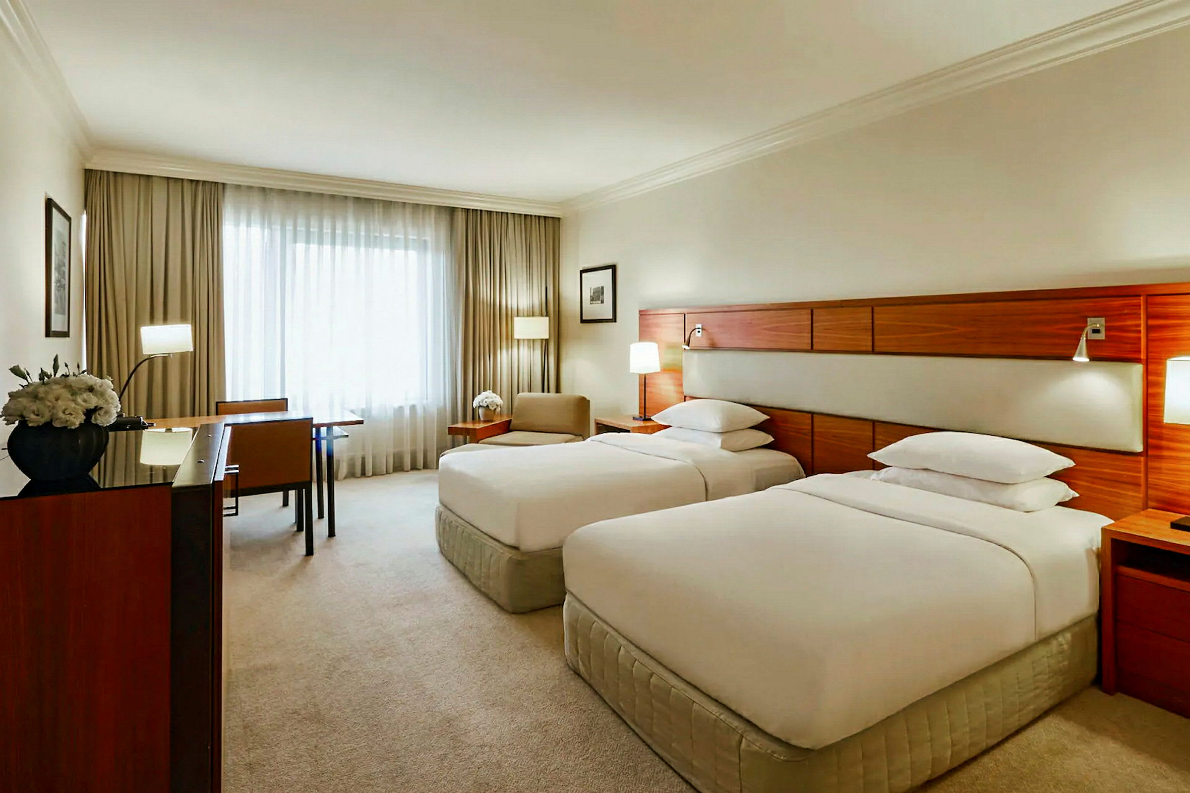 Ett hotellrum med två enkelsängar, ett skrivbord och stol, samt stora fönster med gardiner. (AI-genererad text)