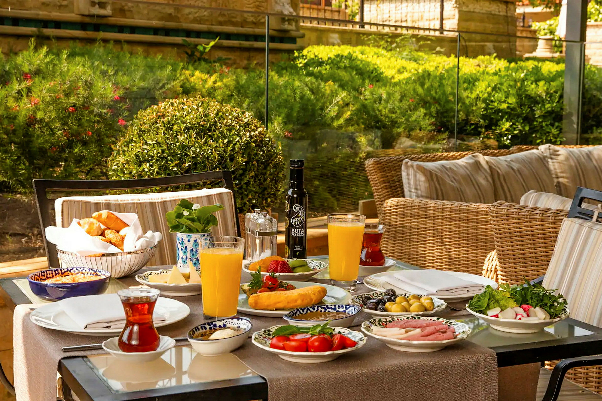 Ett färgglatt frukostbord med olika rätter, juice och te, placerat utomhus med grönska i bakgrunden. (AI-genererad text)