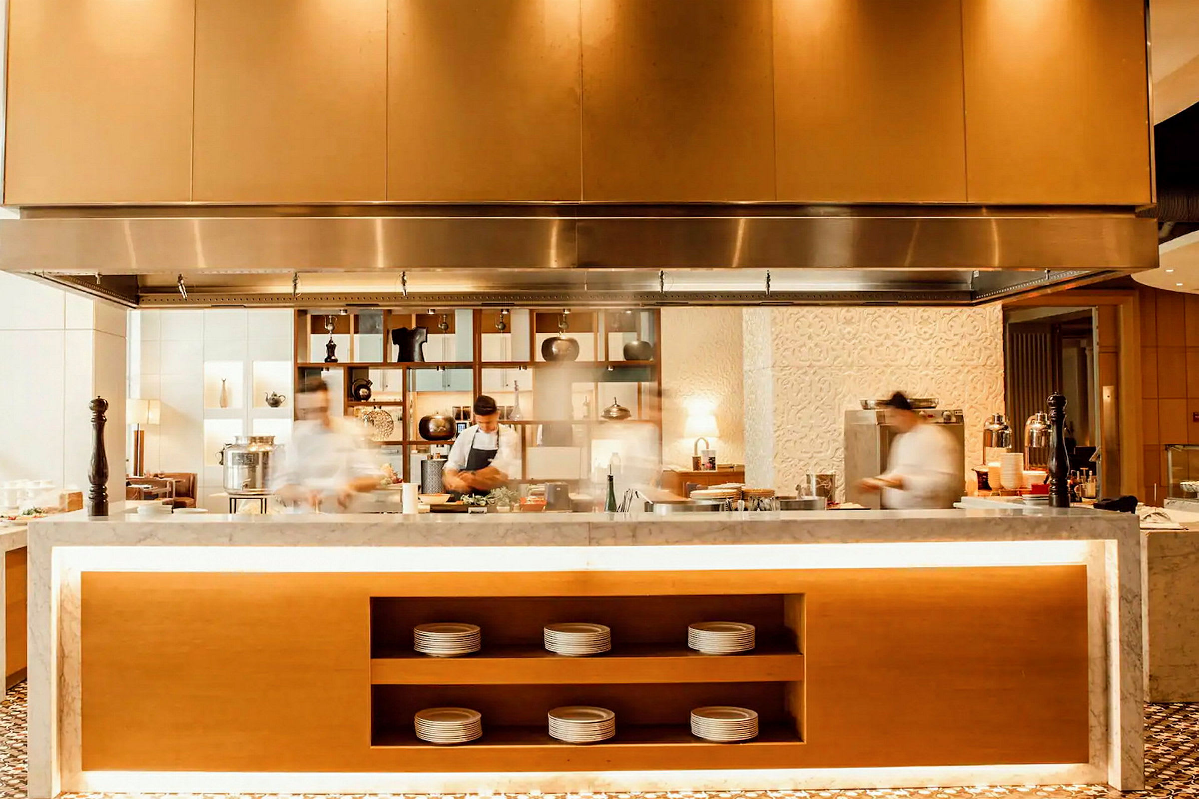 En restaurang med öppen köksmiljö där kockar tillagar mat bakom en marmordisk. (AI-genererad text)