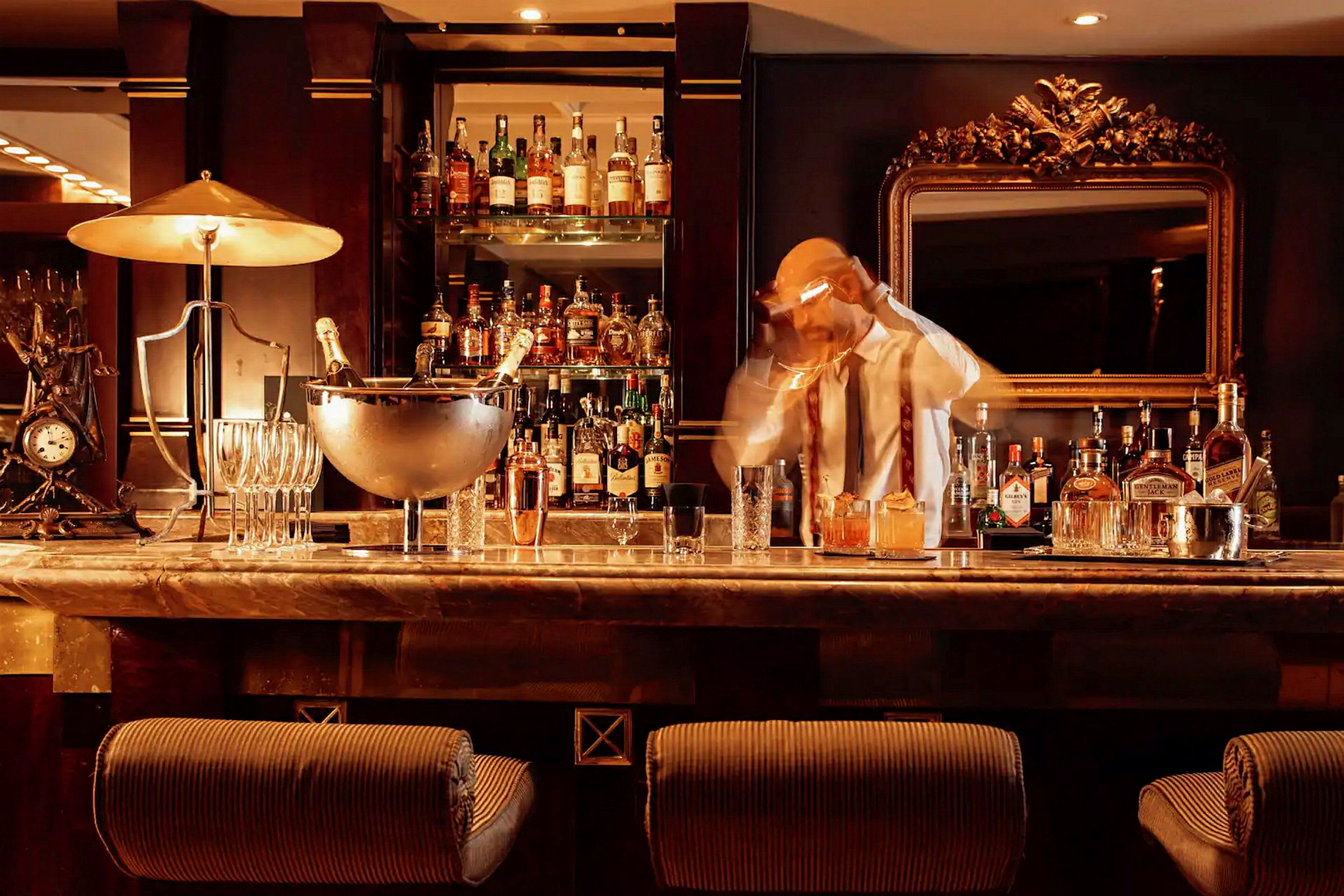 En bartender arbetar i en stilfull bar med flaskor och glas på disken. (AI-genererad text)