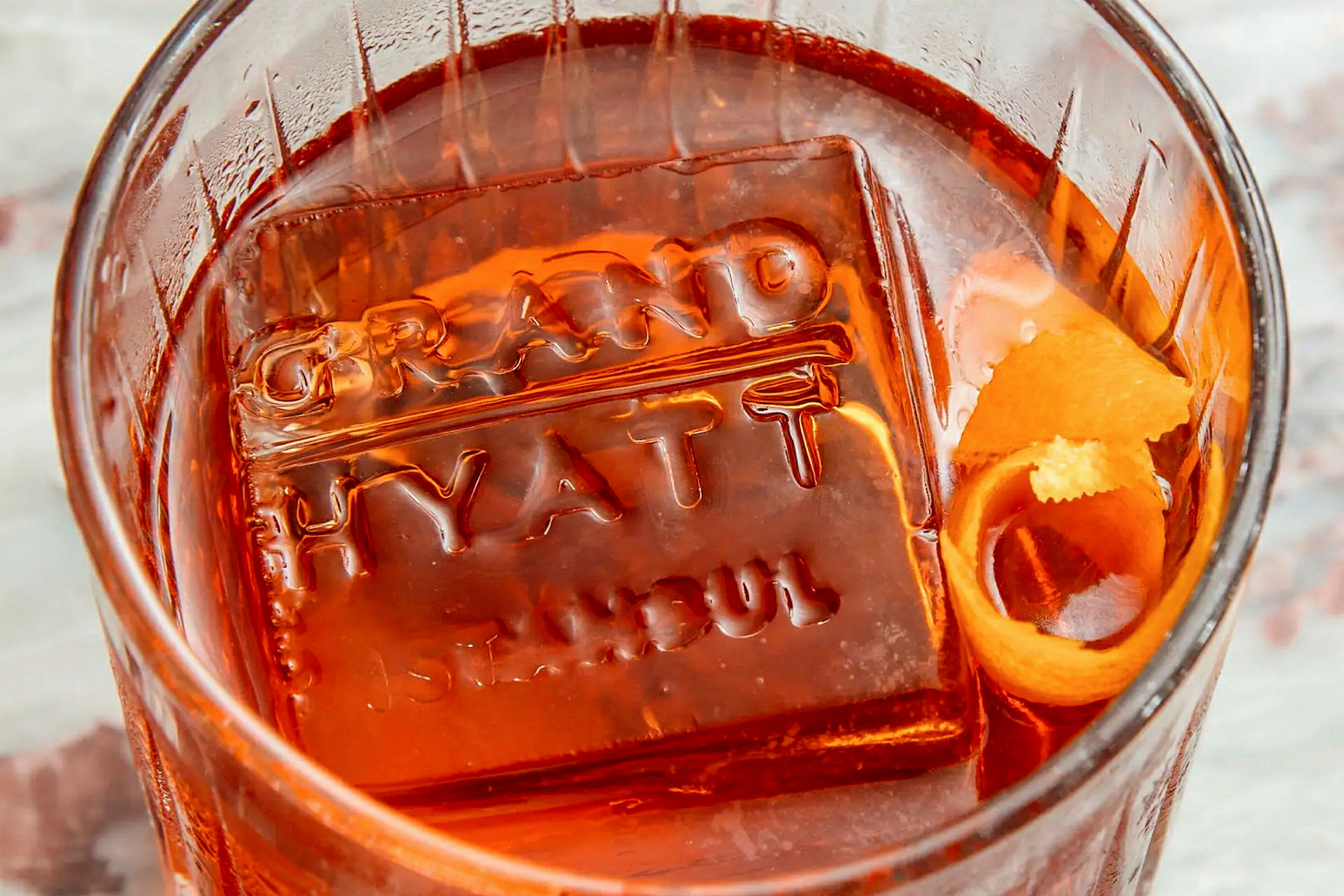 Ett glas med en orange dryck och en isbit präglad med texten 'Grand Hyatt Istanbul'. (AI-genererad text)