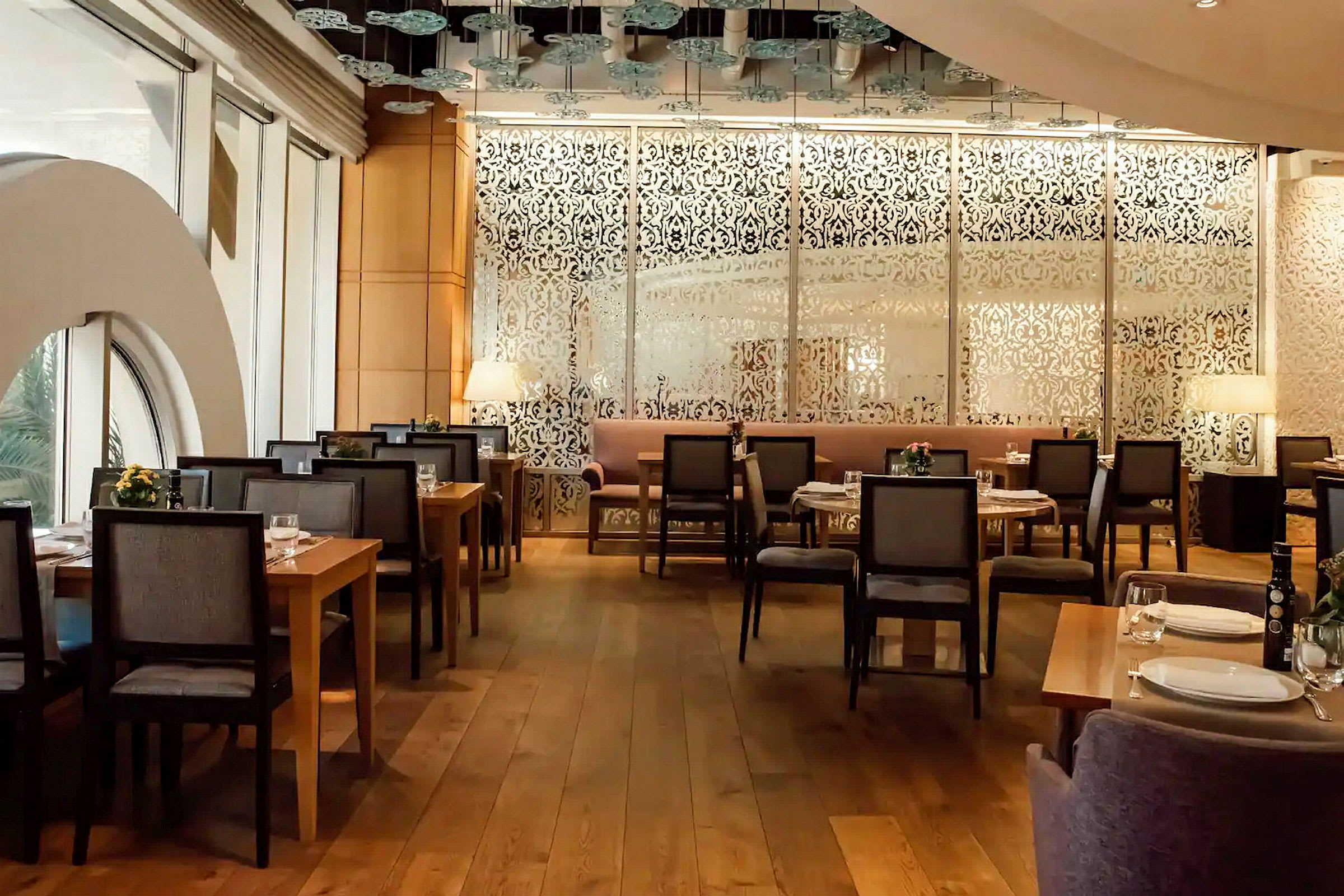 En fin restaurang med dekorativa mönstrade skärmar och träbord omgivna av stolar. (AI-genererad text)