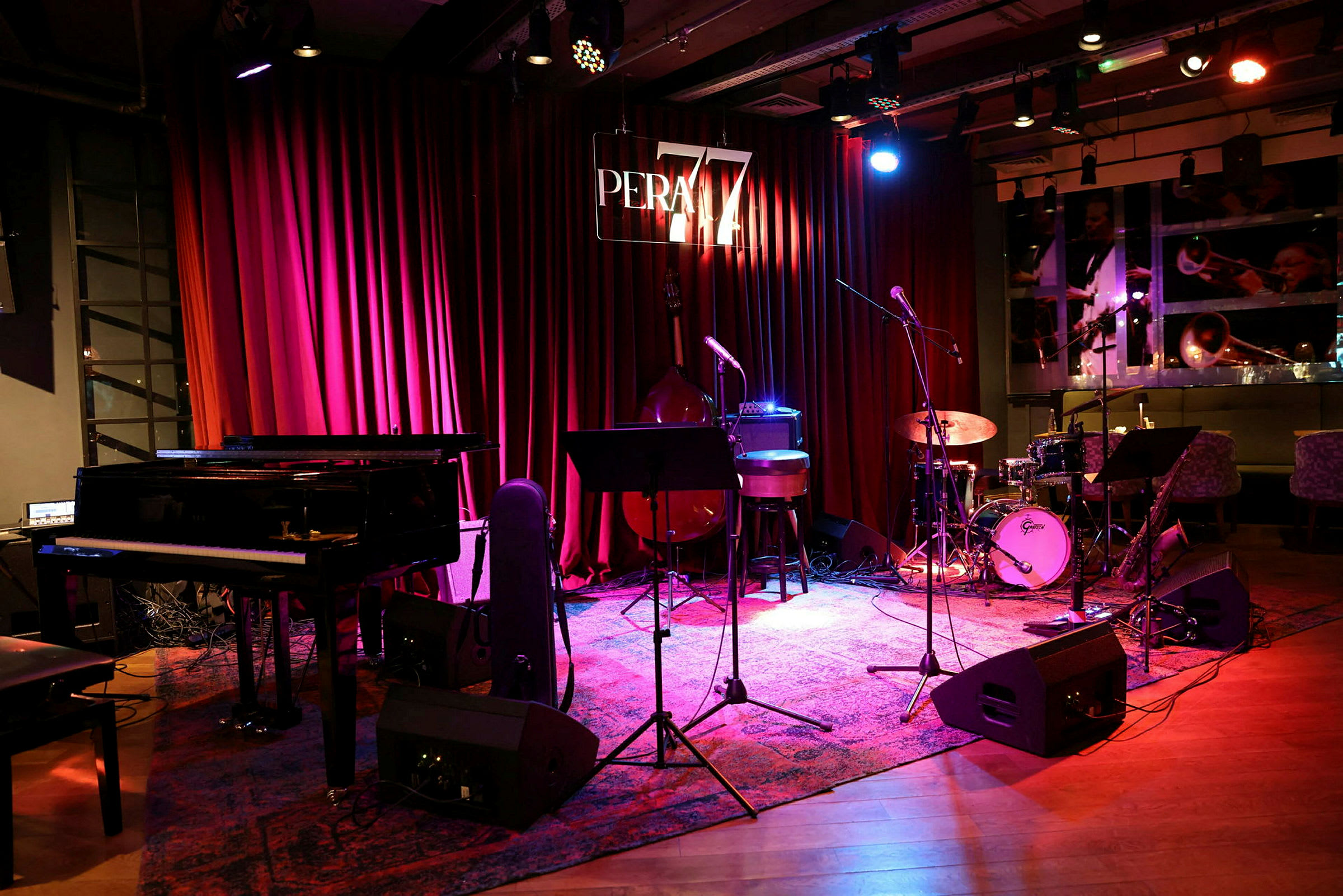 Scen med piano, mikrofoner, trumset och andra instrument framför röda gardiner. (AI-genererad text)