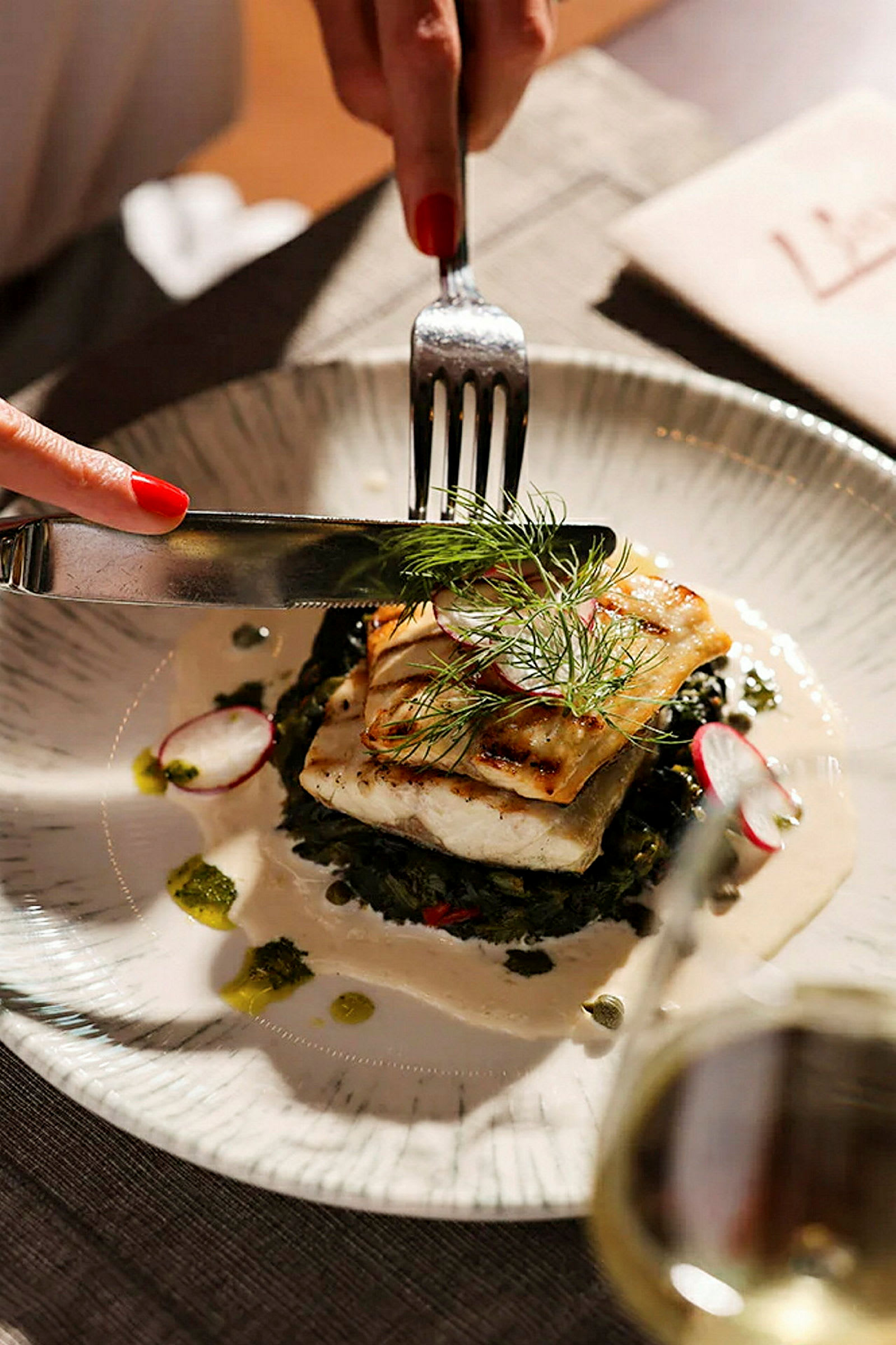En tallrik med en måltid bestående av grillad fisk, serverad med grönsaker och en sås. Bestick används på maten. (AI-genererad text)