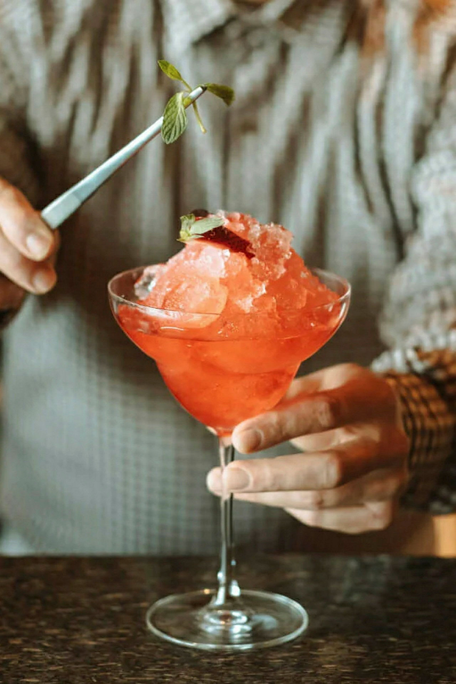 En person håller i ett glas med röd slush, dekorerar med mintblad. (AI-genererad text)