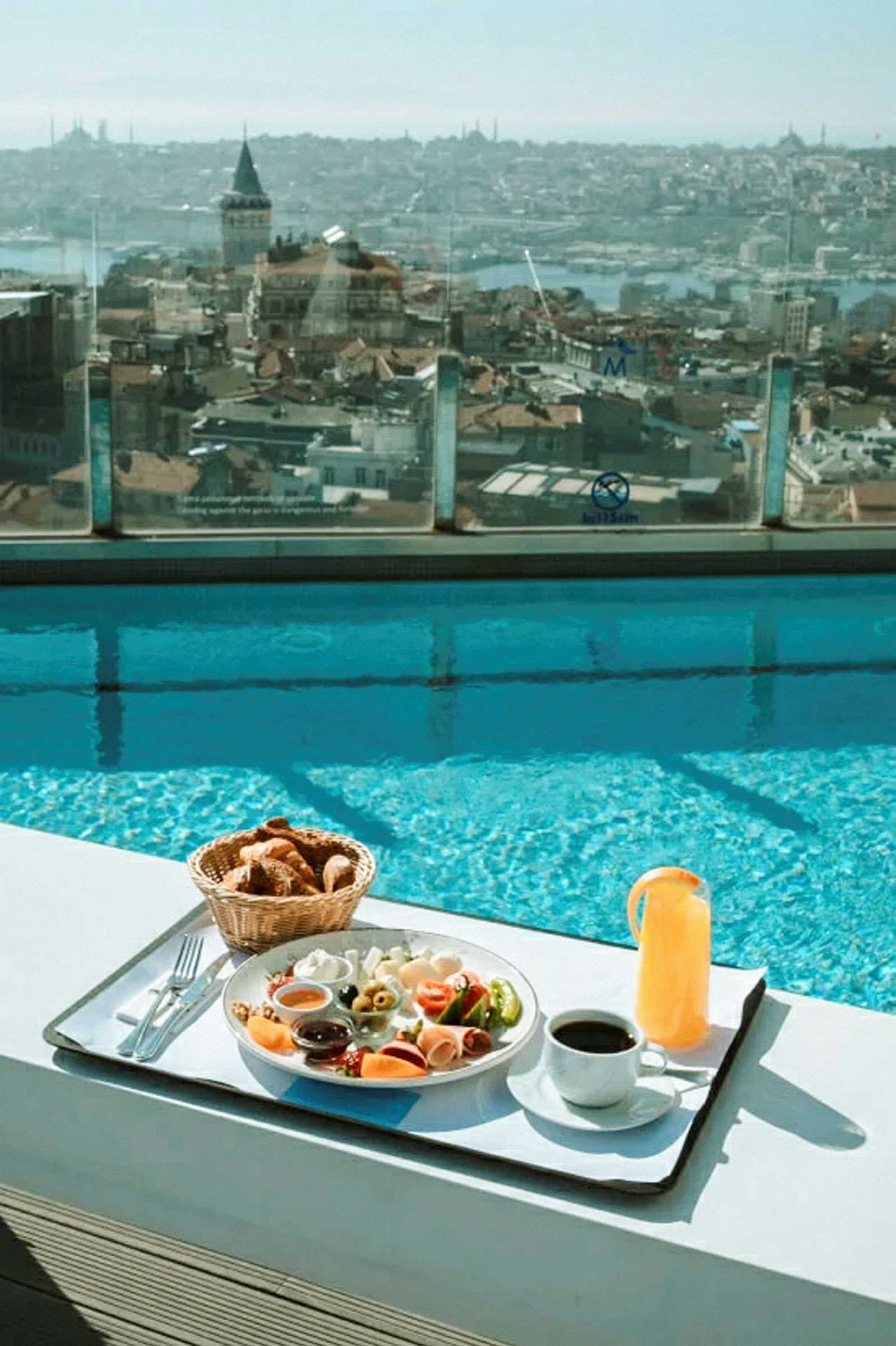 Frukost serverad vid kanten av en pool med utsikt över stadens hustak och Galatatornet. (AI-genererad text)