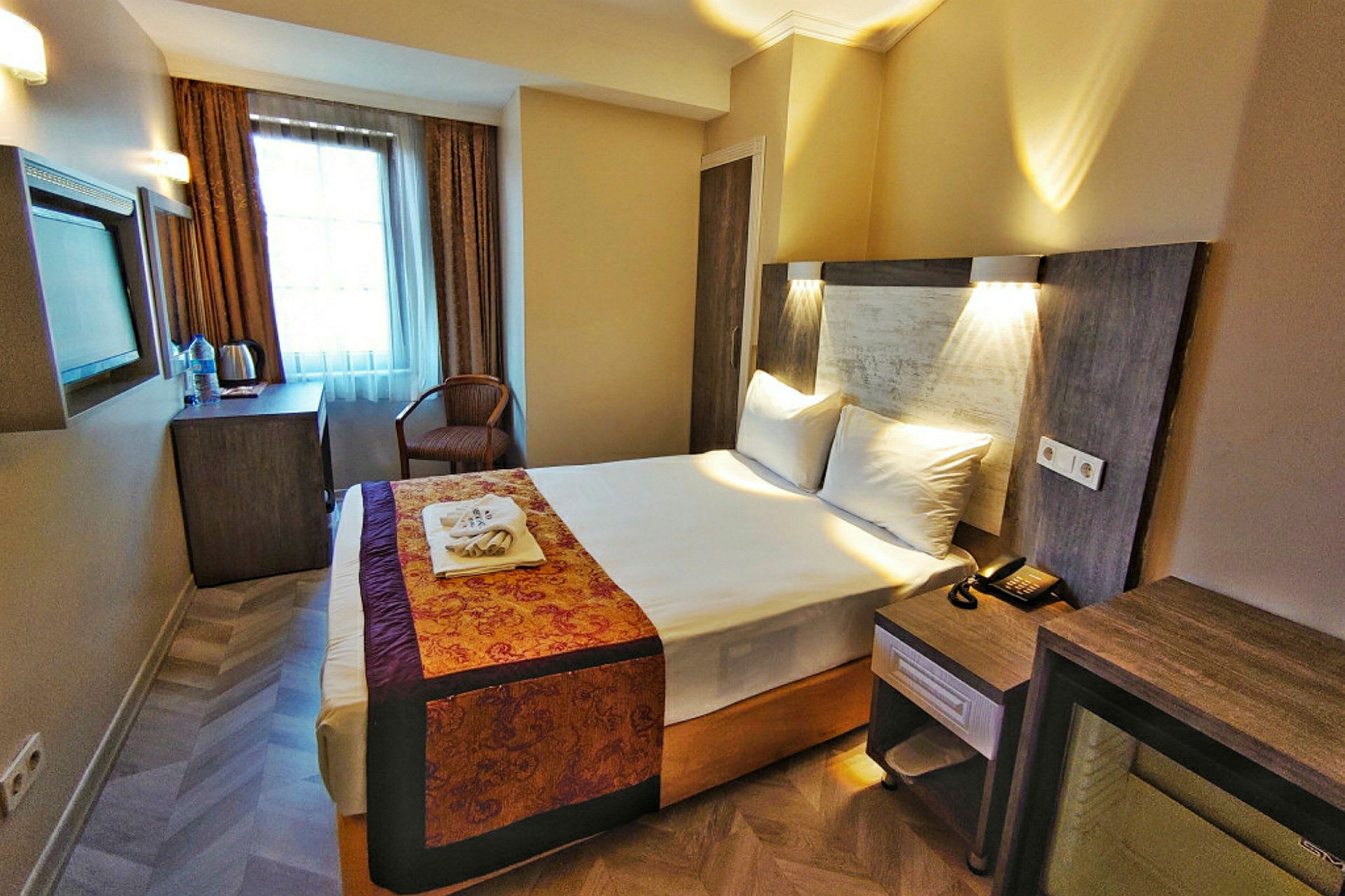 Ett hotellrum med en bäddad dubbelsäng. Det finns skrivbord, stol och fönster med gardiner. (AI-genererad text)