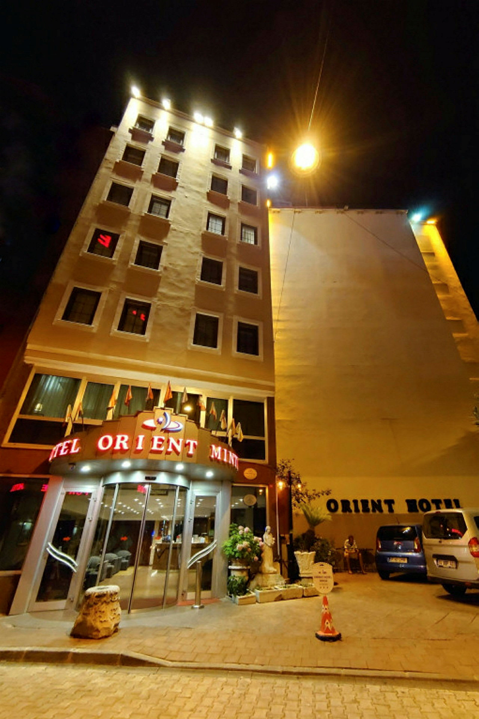 Ett hotell vid natt, med skyltar och belysning på fasaden samt parkerade bilar utanför. (AI-genererad text)