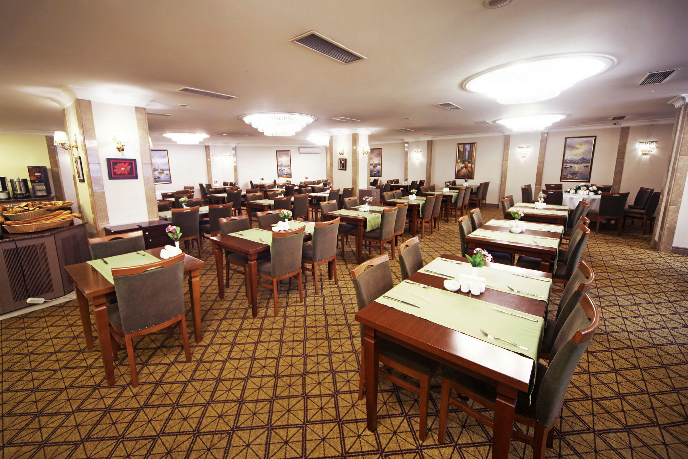 Restaurang med flera uppställda bord och stolar, dukade med gröna underlägg och blomdekorationer. (AI-genererad text)