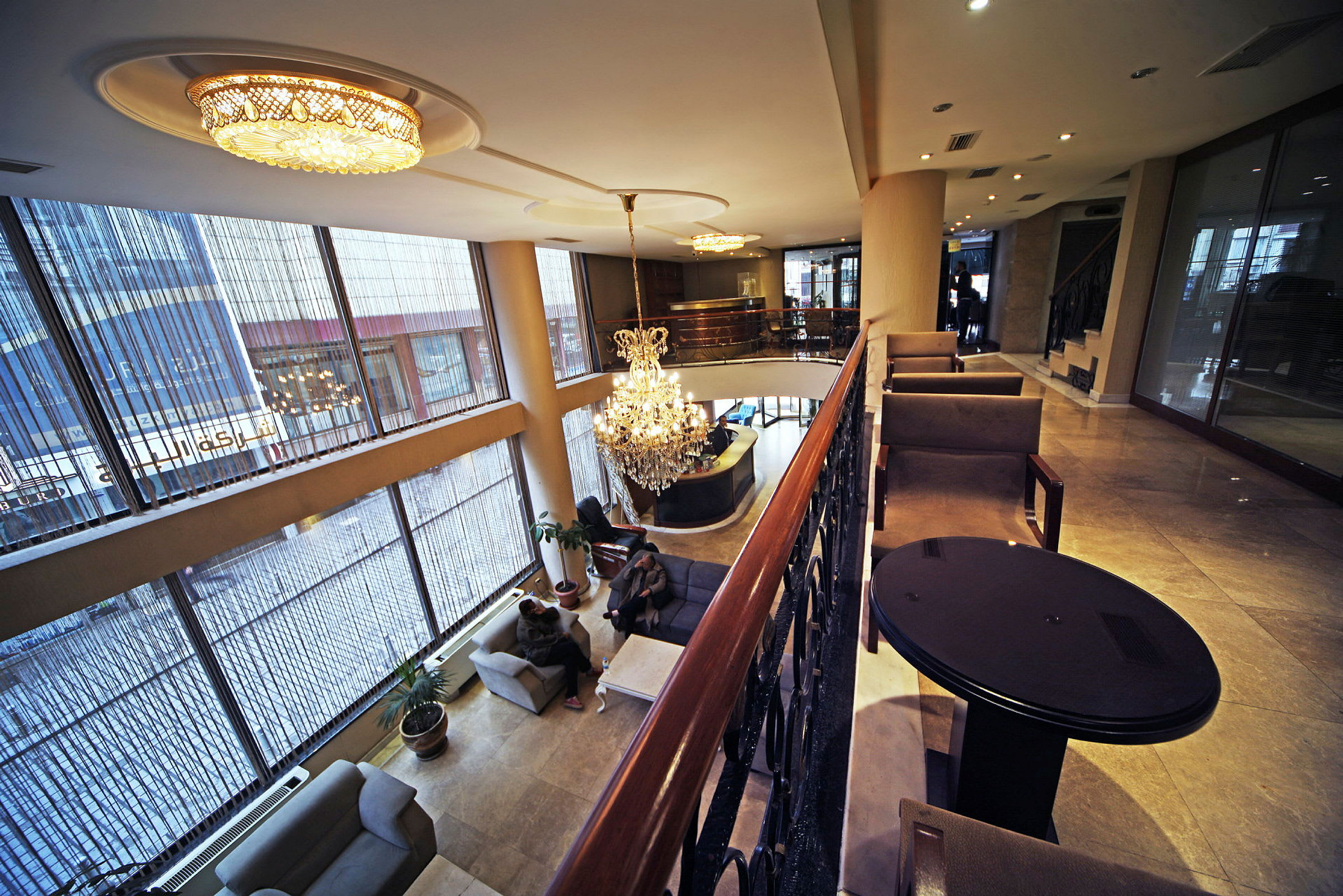 Bild av en hotelllobby med stora glasfönster, taklampor och en kristallkrona. Möblerade sittplatser finns på olika nivåer. (AI-genererad text)