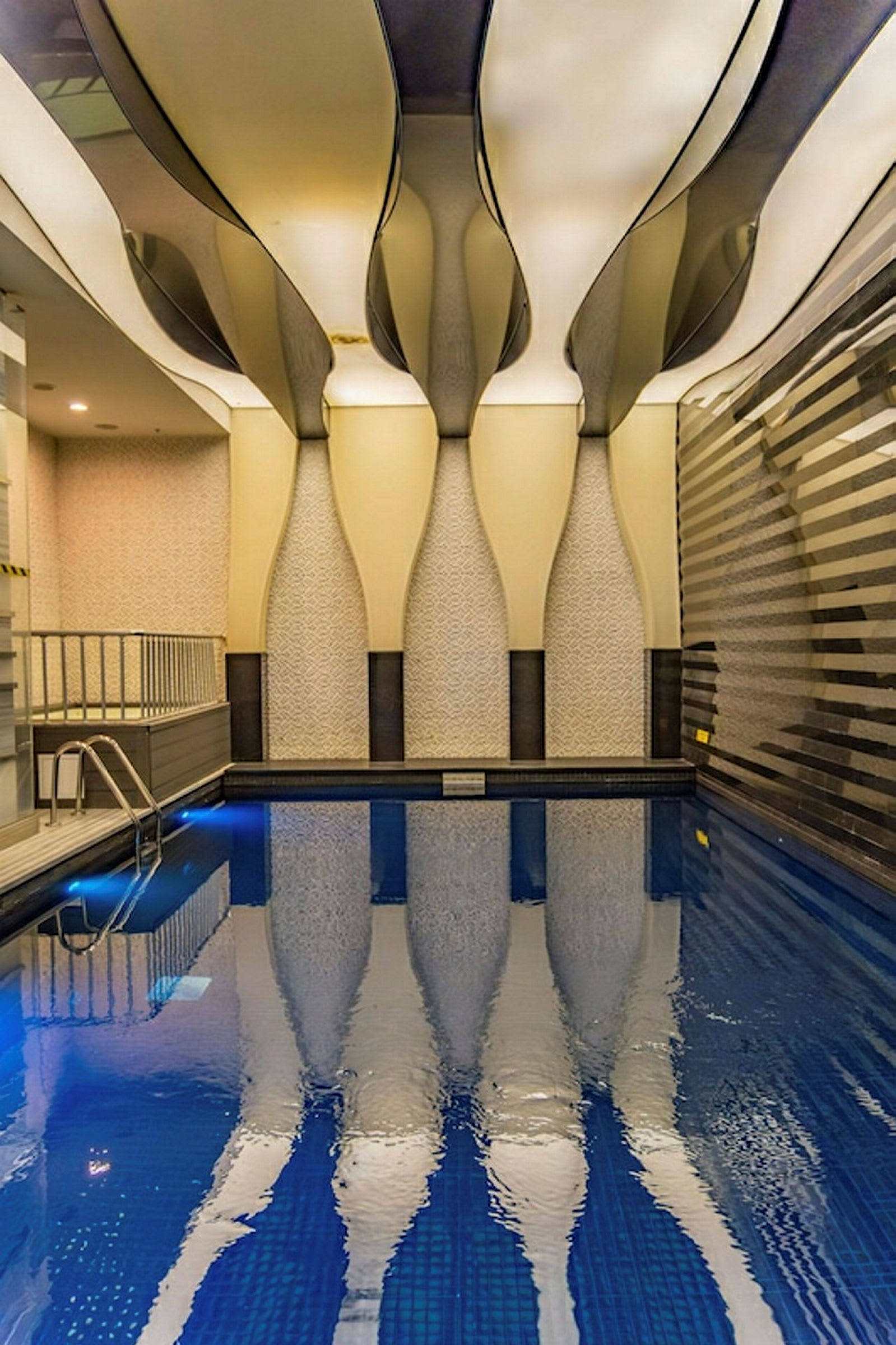 En inomhuspool med unikt designat tak och mönstrade väggar. Vattnet speglar arkitekturen ovanför. (AI-genererad text)