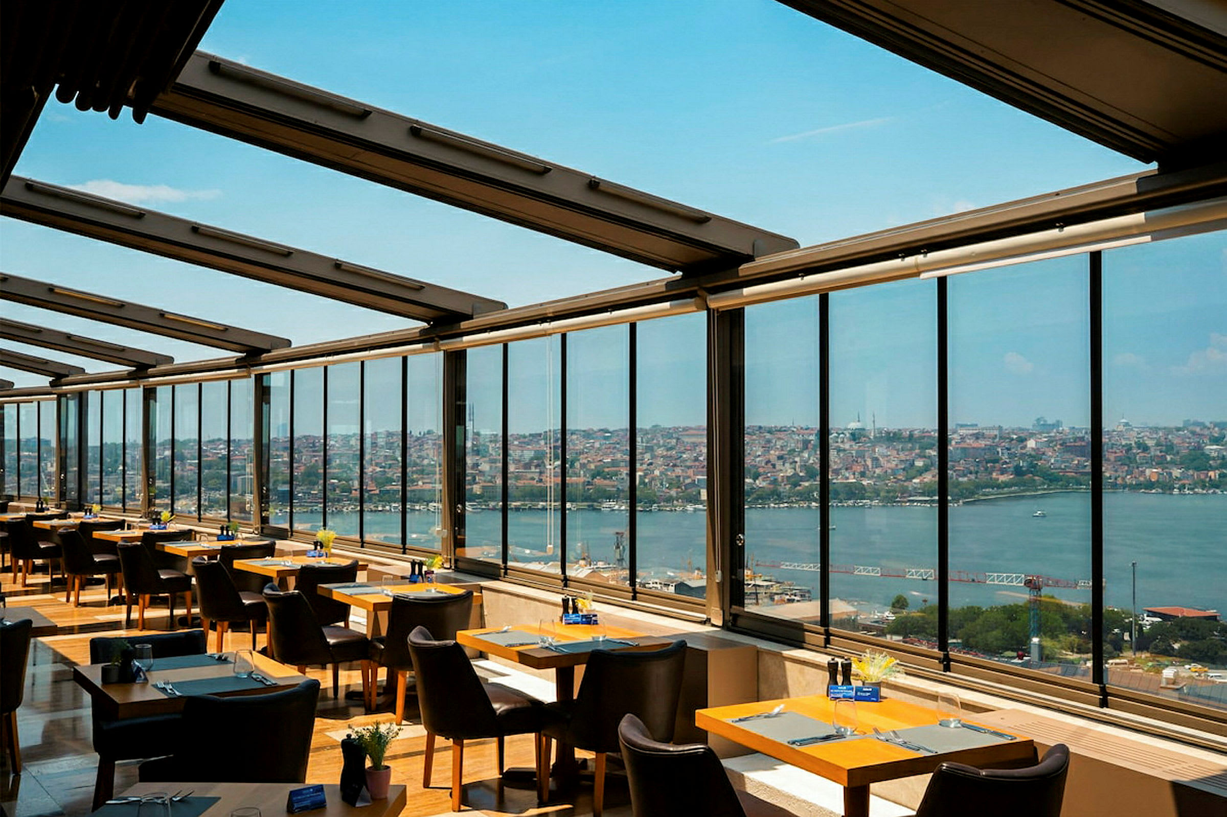 En restaurang med stora fönster som har utsikt mot en stad och ett vattendrag. (AI-genererad text)