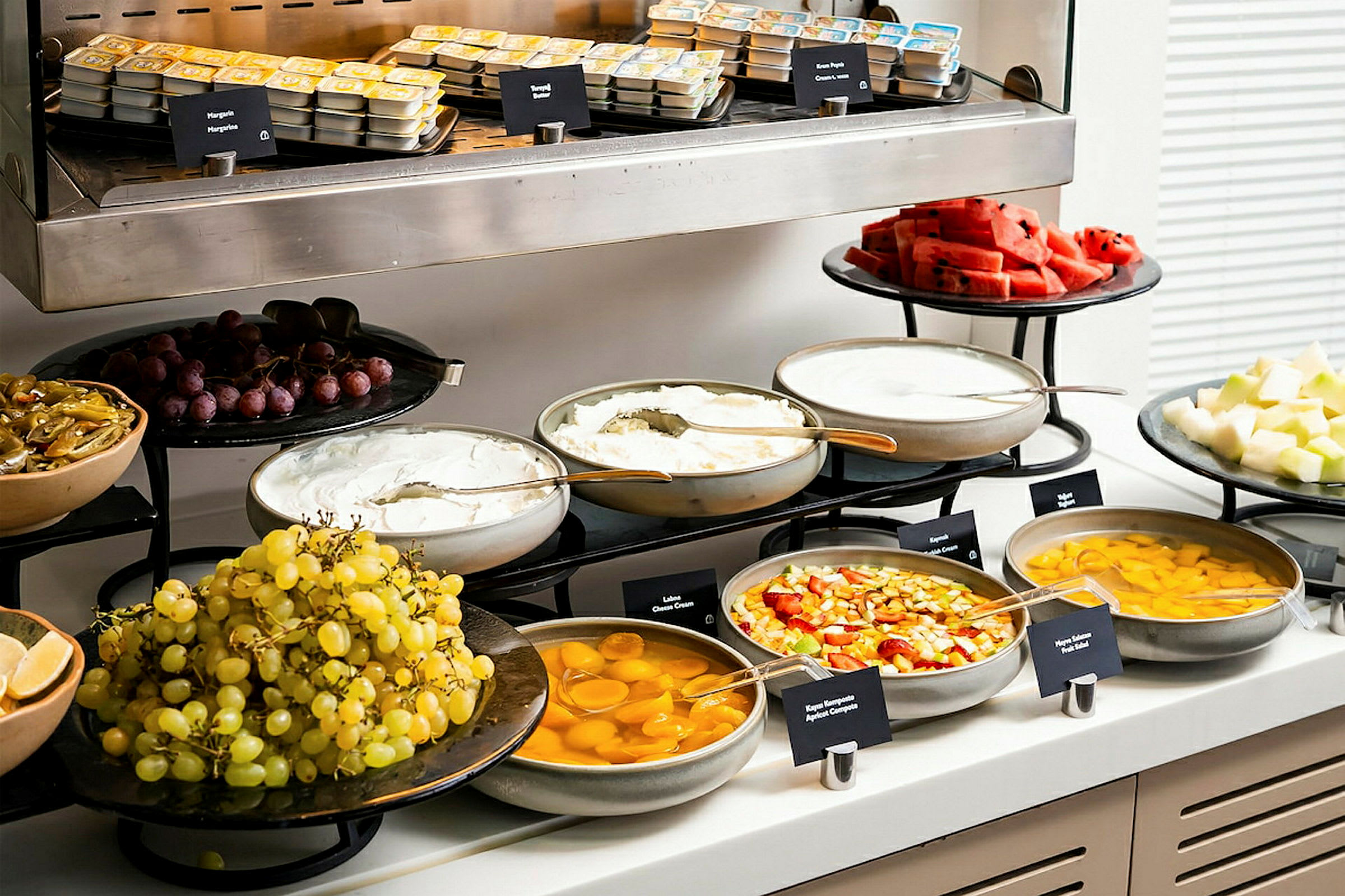 Ett buffébord med ett urval av frukter, yoghurt, konserverad frukt och smörförpackningar. (AI-genererad text)