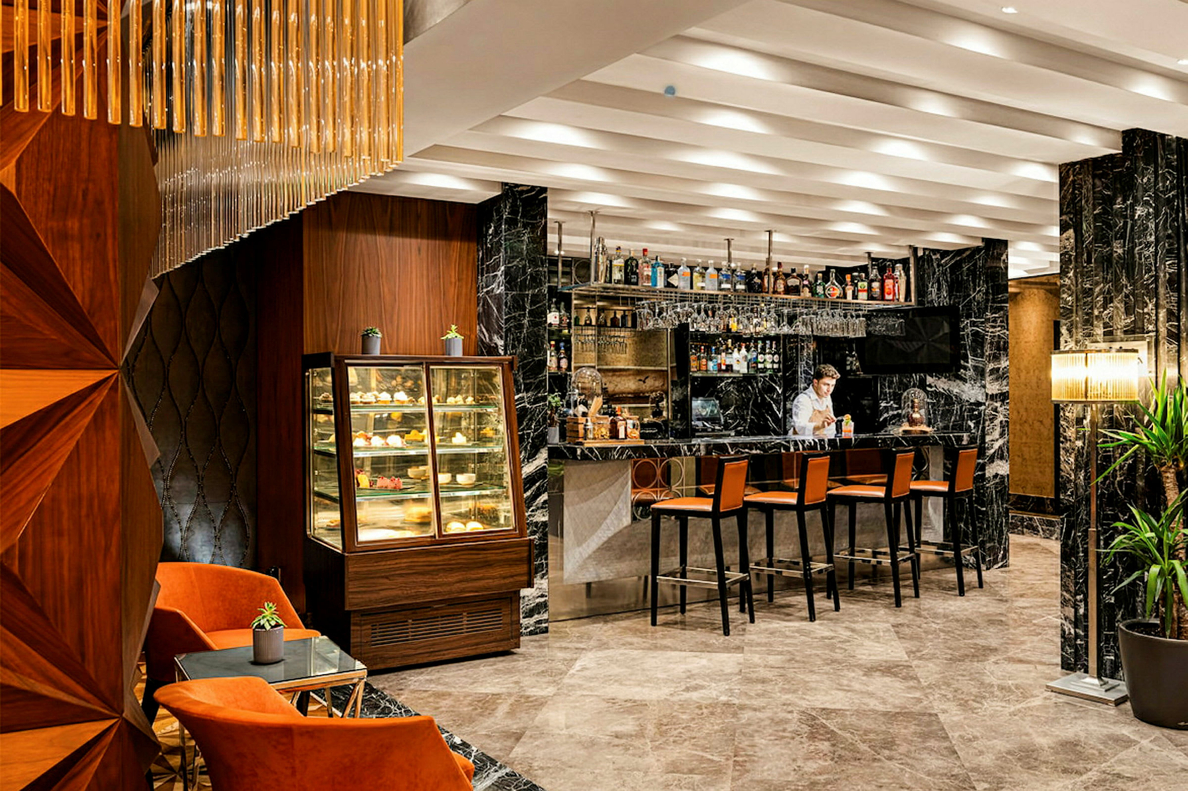 Interiör av en elegant bar med marmordetaljer, en alkoholdryckskollektion på hyllorna, stolar vid baren och en displayer för bakverk. (AI-genererad text)