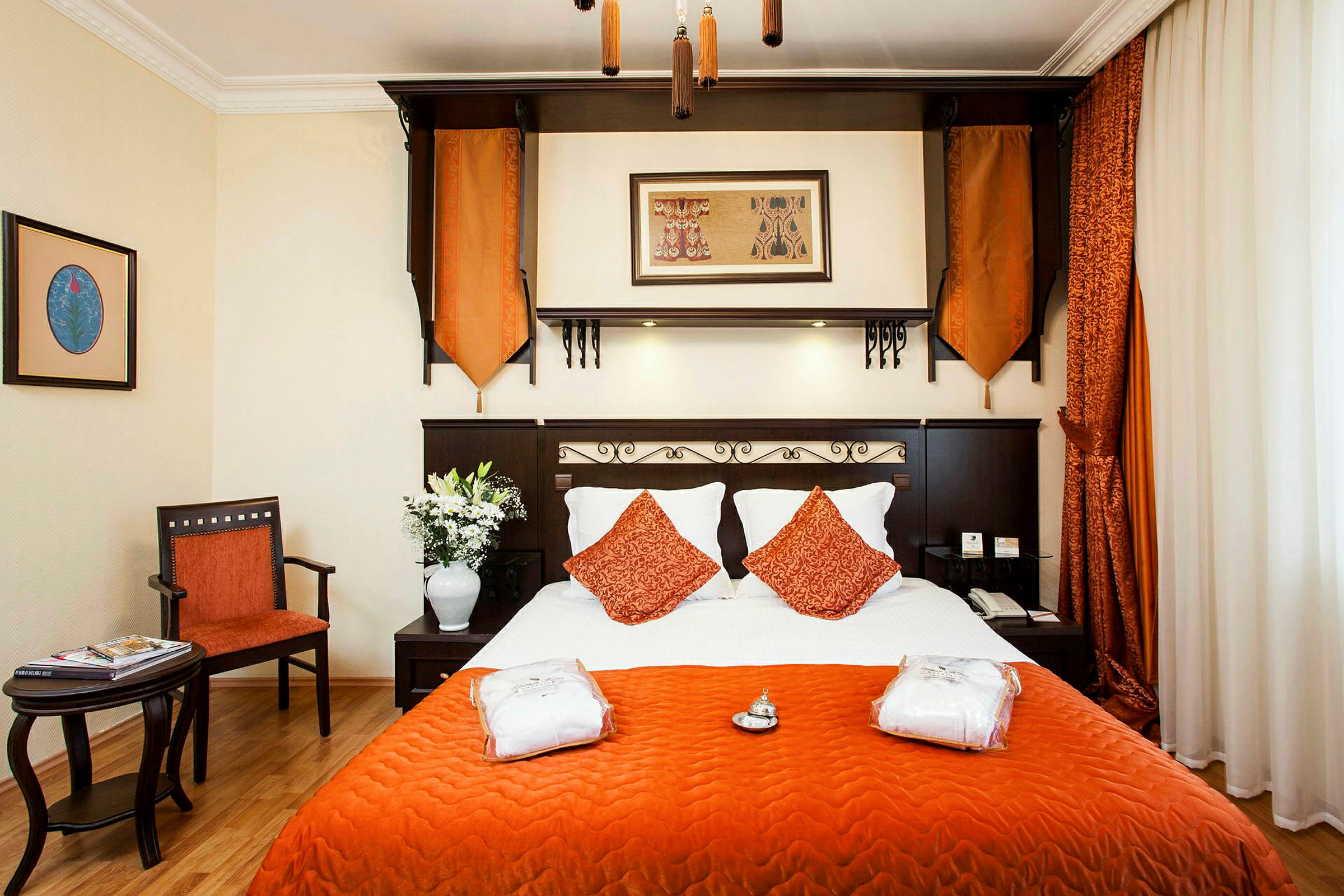 Ett hotellrum med en säng klädd i vitt och orange, omgiven av möbler och dekorationer. (AI-genererad text)