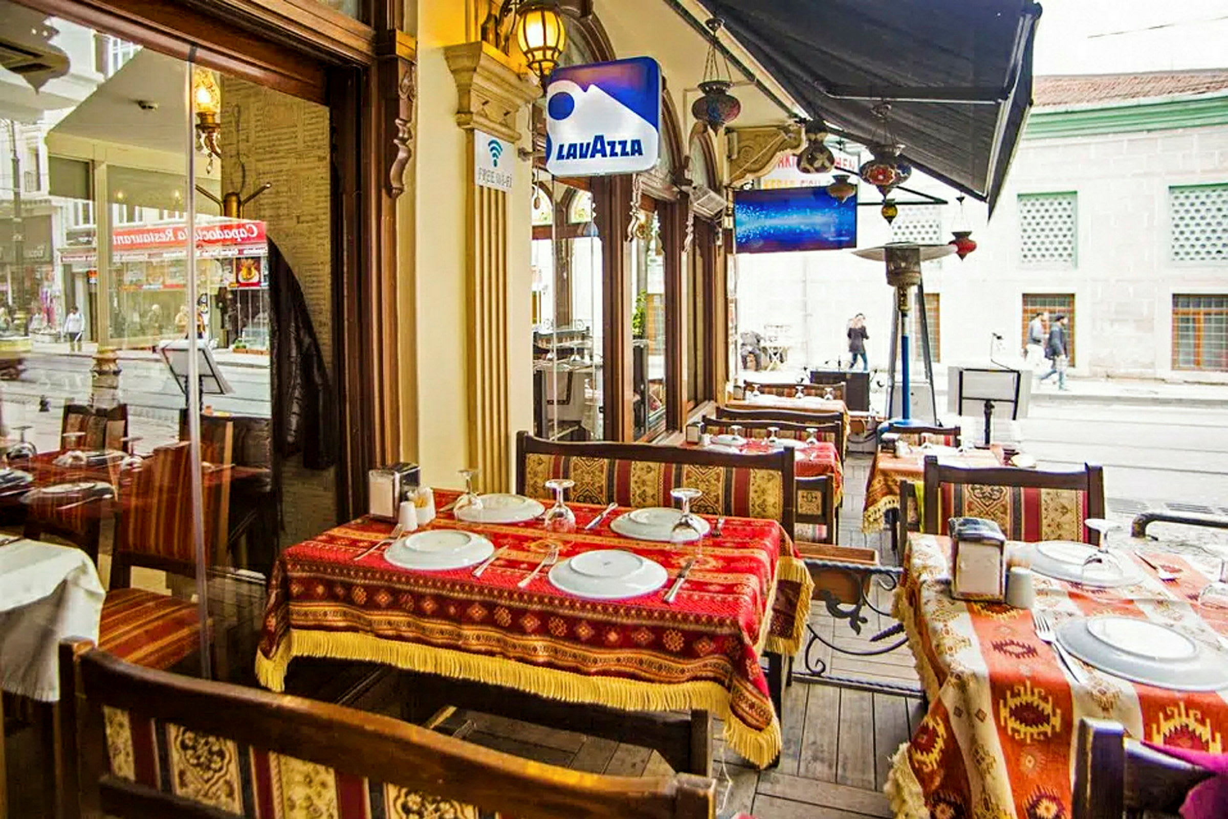 En utomhusservering vid en restaurang med bord, stolar och dukar med mönster. (AI-genererad text)