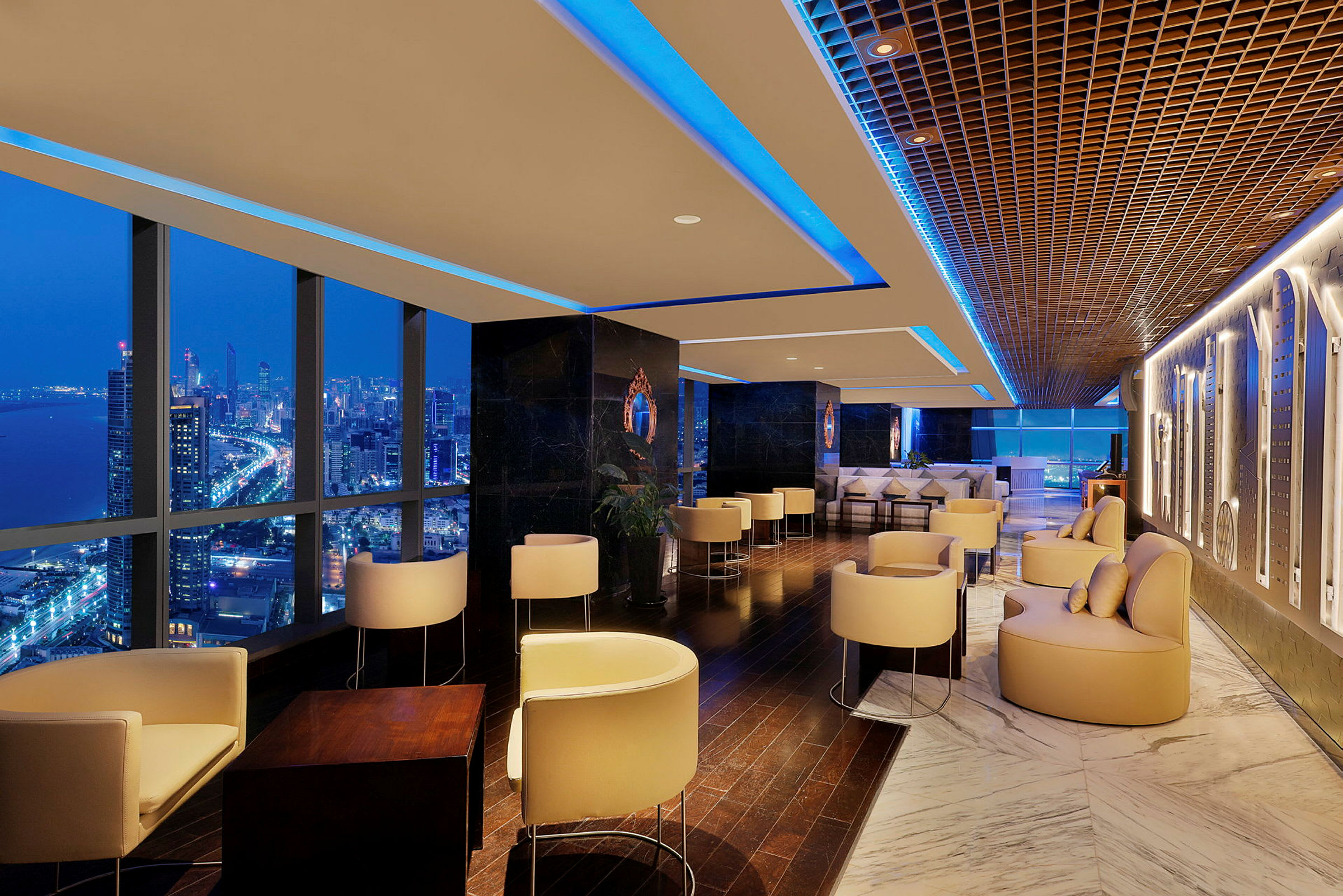 En elegant lounge med moderna möbler och stora fönster som visar en kvällsutsikt över en stad. (AI-genererad text)