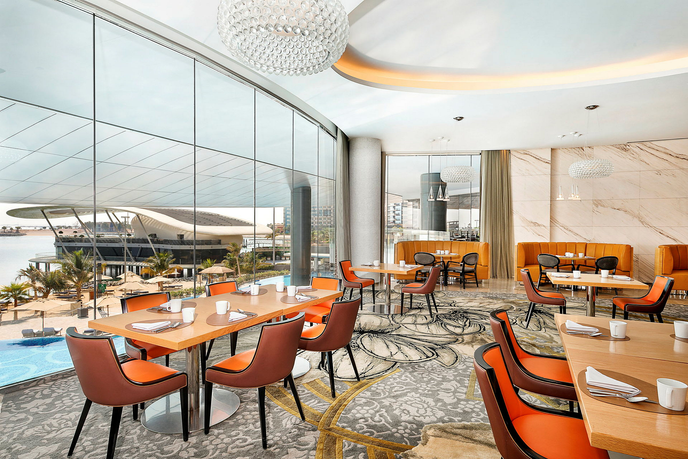 Ett modernt restaurangområde med stora glasfönster som visar utsikten över en pool och ett futuristiskt byggnadskomplex. (AI-genererad text)